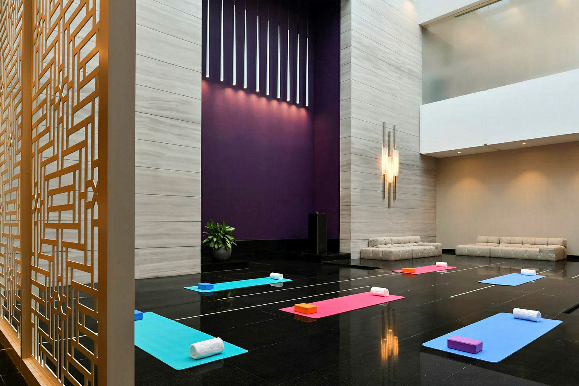 Ett rum med yogamattor och tillhörande tillbehör uppställda på ett blankt golv. Det finns moderna soffor vid sidan och en dekorativ galleravskiljare. (AI-genererad text)