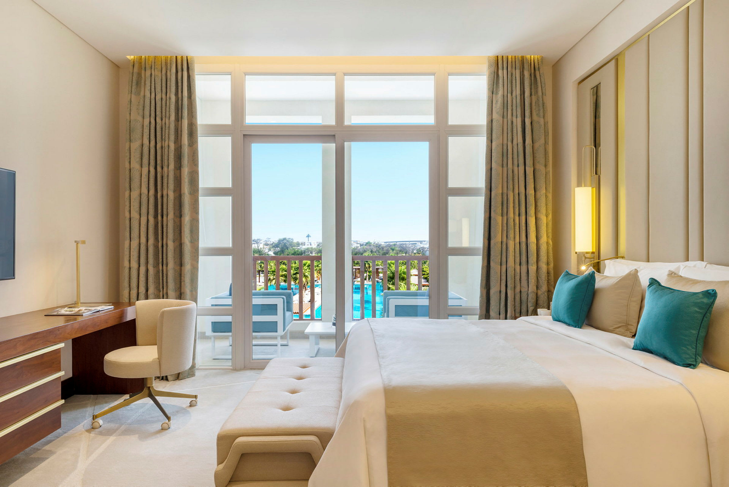 Ett modernt hotellrum med en stor säng, skrivbord, sittmöble och balkong med utsikt över en pool. (AI-genererad text)