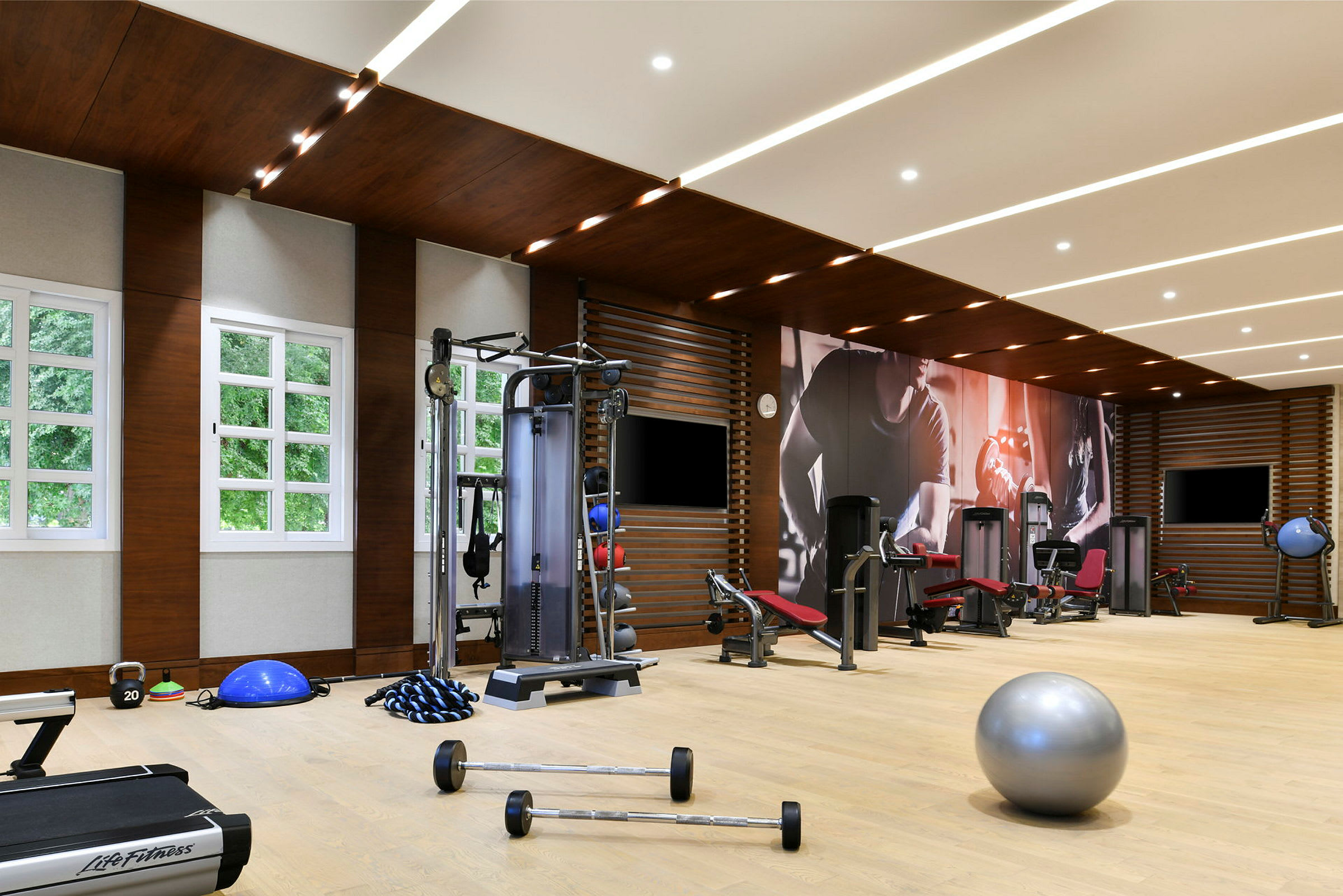 Ett gym med träningsredskap och maskiner samt ljusa fönster. (AI-genererad text)