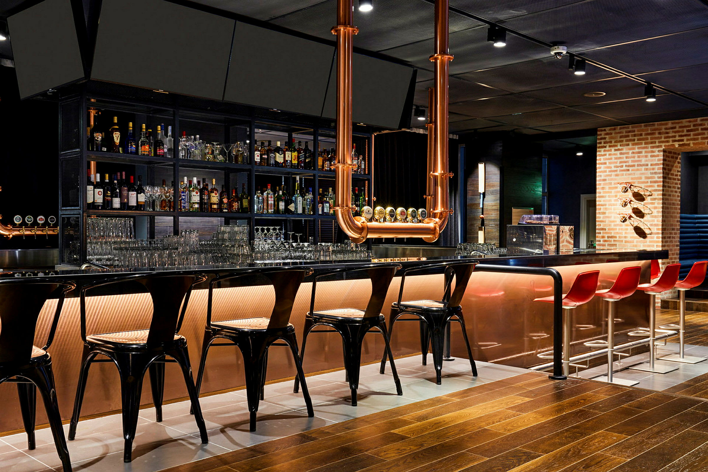 En modern bar med en lång bardisk, höga stolar och flaskor uppställda i hyllor bakom. (AI-genererad text)