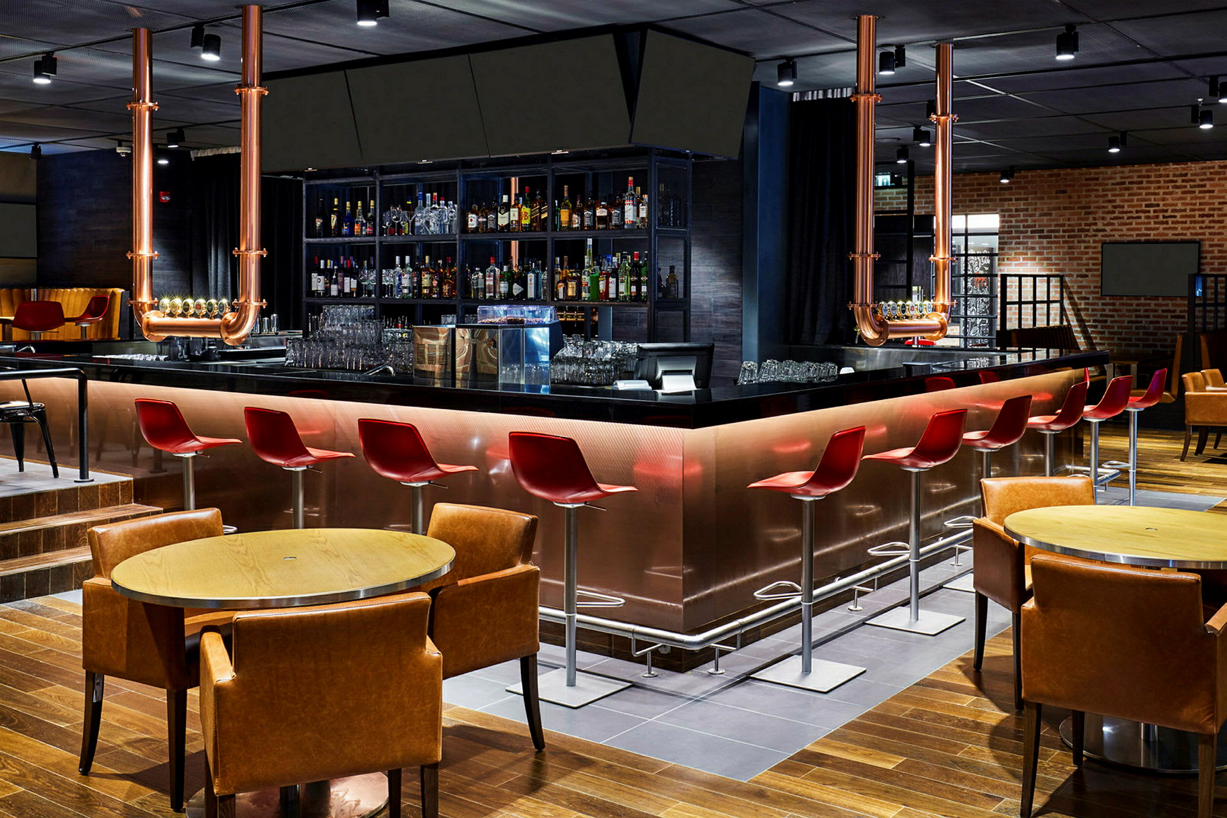 En modern bar med röda stolar, ett blankt svart bardisk, och en rad spritflaskor på hyllorna bakom. (AI-genererad text)