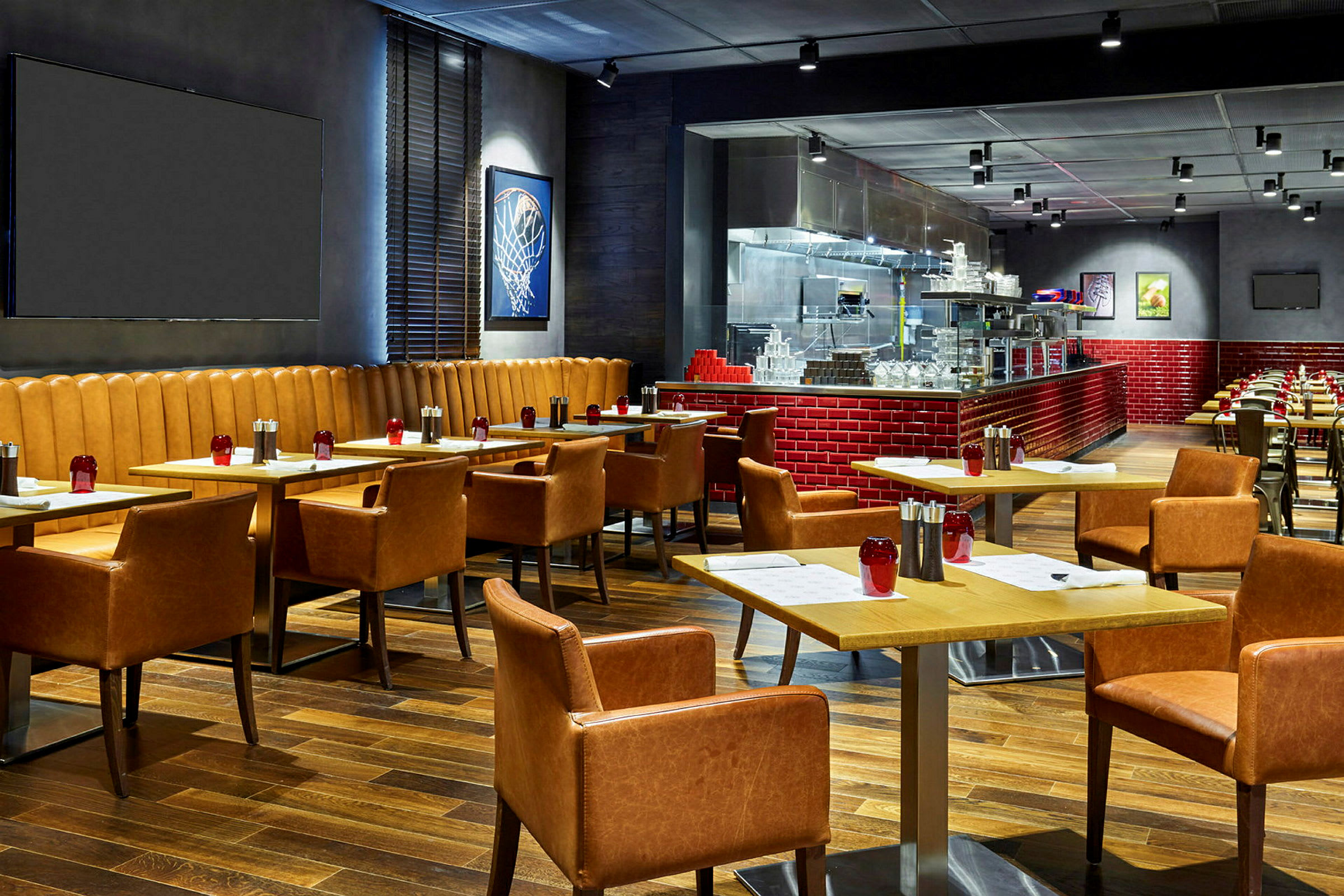 En modern restaurang med träbord och bekväma läderstolar. Väggarna dekorerade med konst och öppet kök med röda kakelplattor. (AI-genererad text)