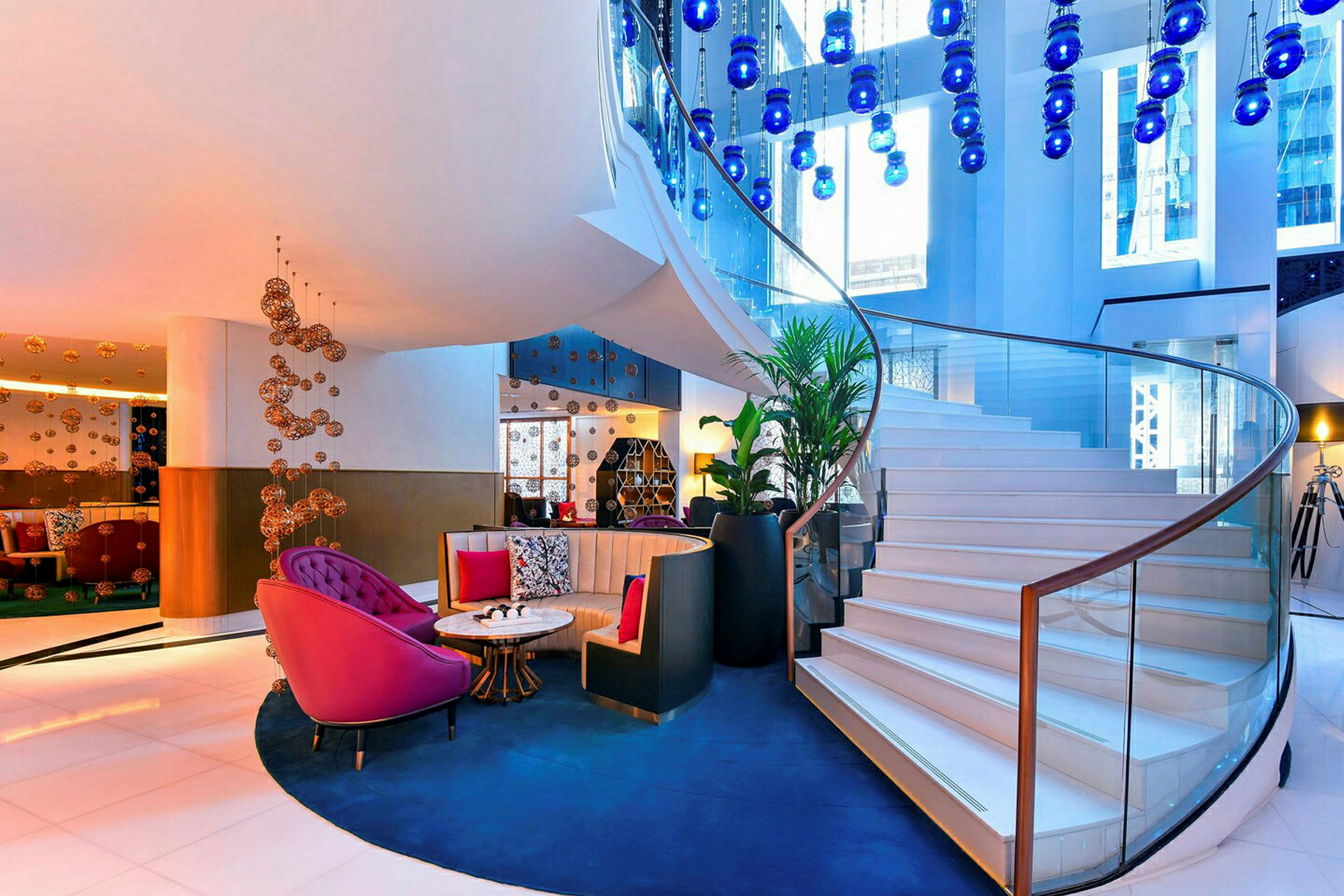 Ljus och elegant hotellobby med spiraltrappa och dekorativa blå lampor. (AI-genererad text)