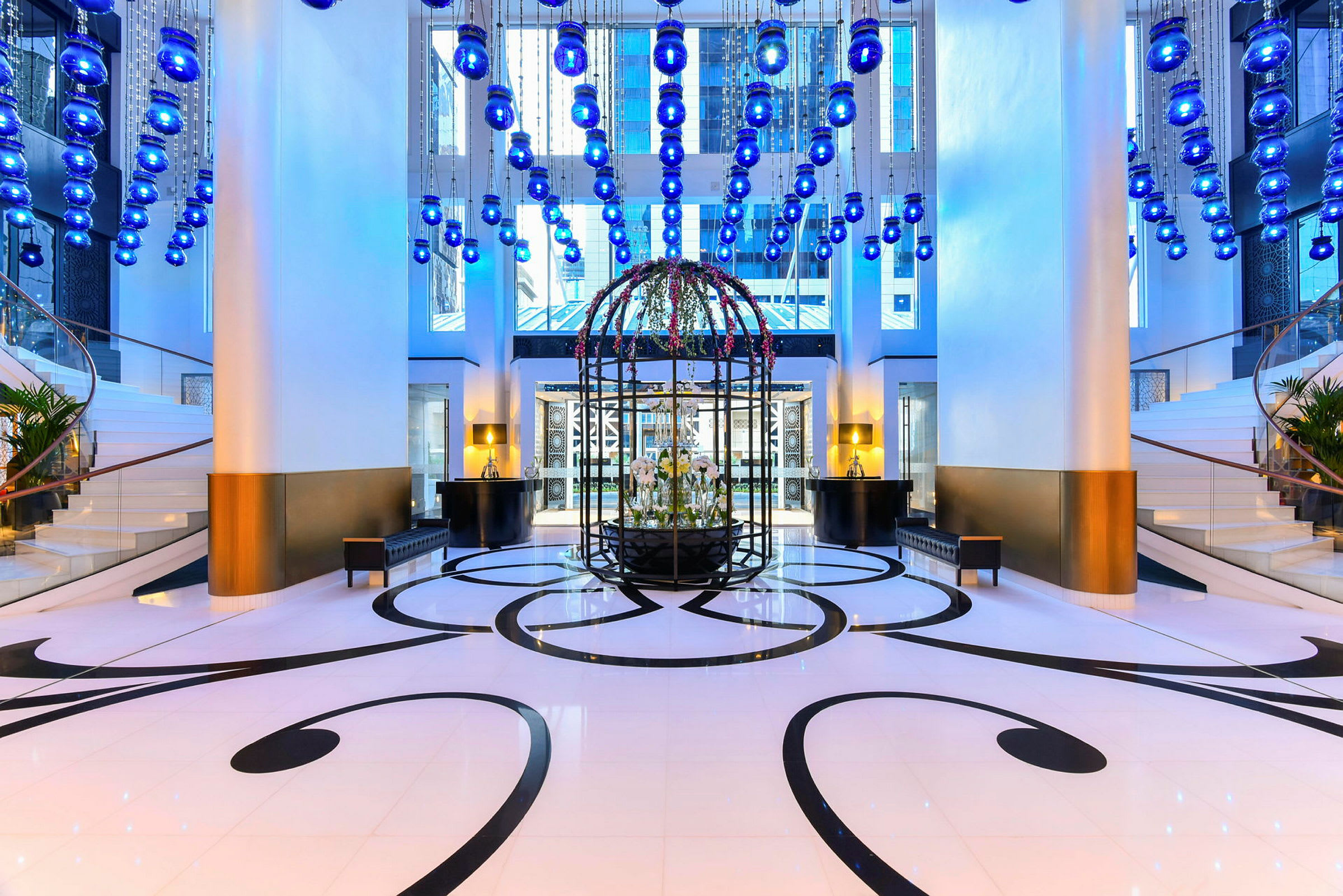 Hotellets lobby med en rund prydnad i mitten och blå hängande lampor i taket. (AI-genererad text)