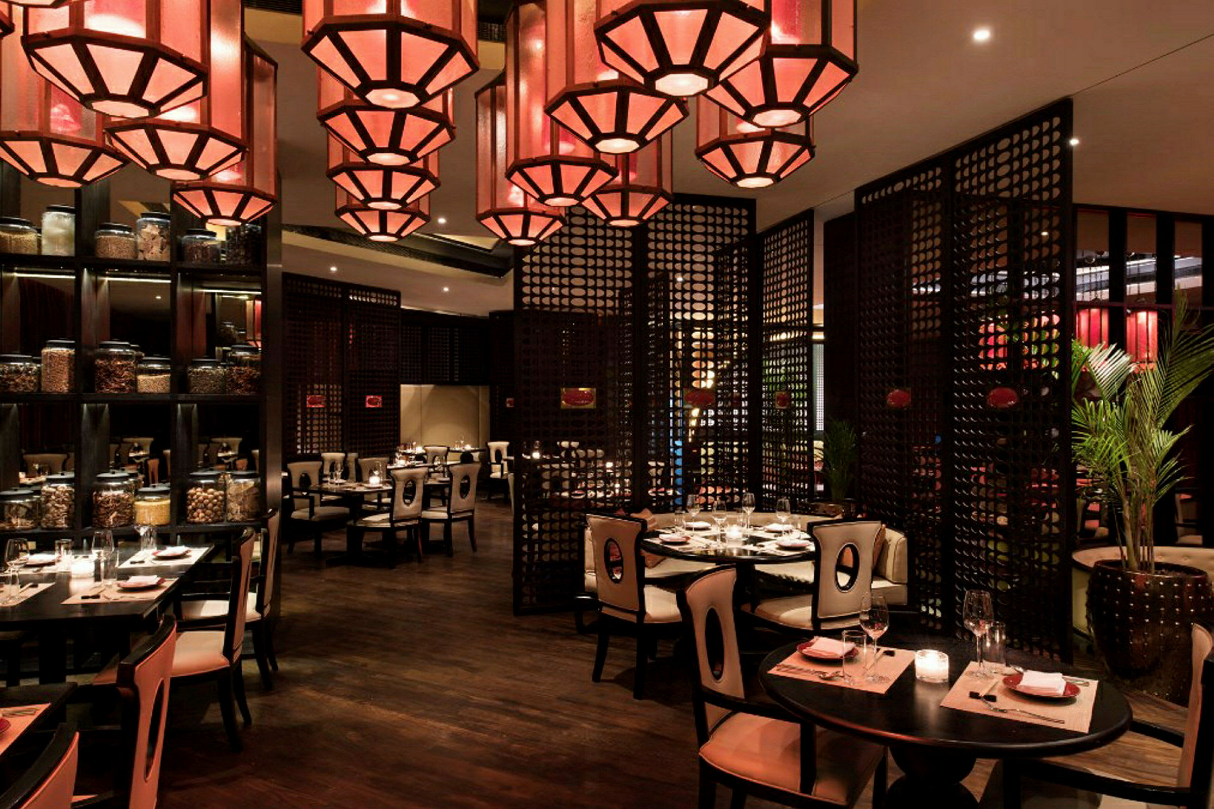 En restaurang med elegant inredning, bord med dukar och stolar samt dekorativa röda lampor i taket. (AI-genererad text)