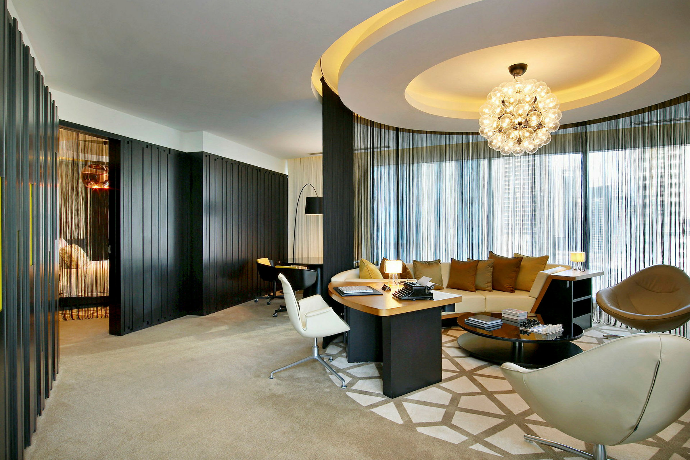 Ett elegant hotellrum med modern möblering, inklusive en rund soffa, skrivbord och dekorativ belysning. (AI-genererad text)