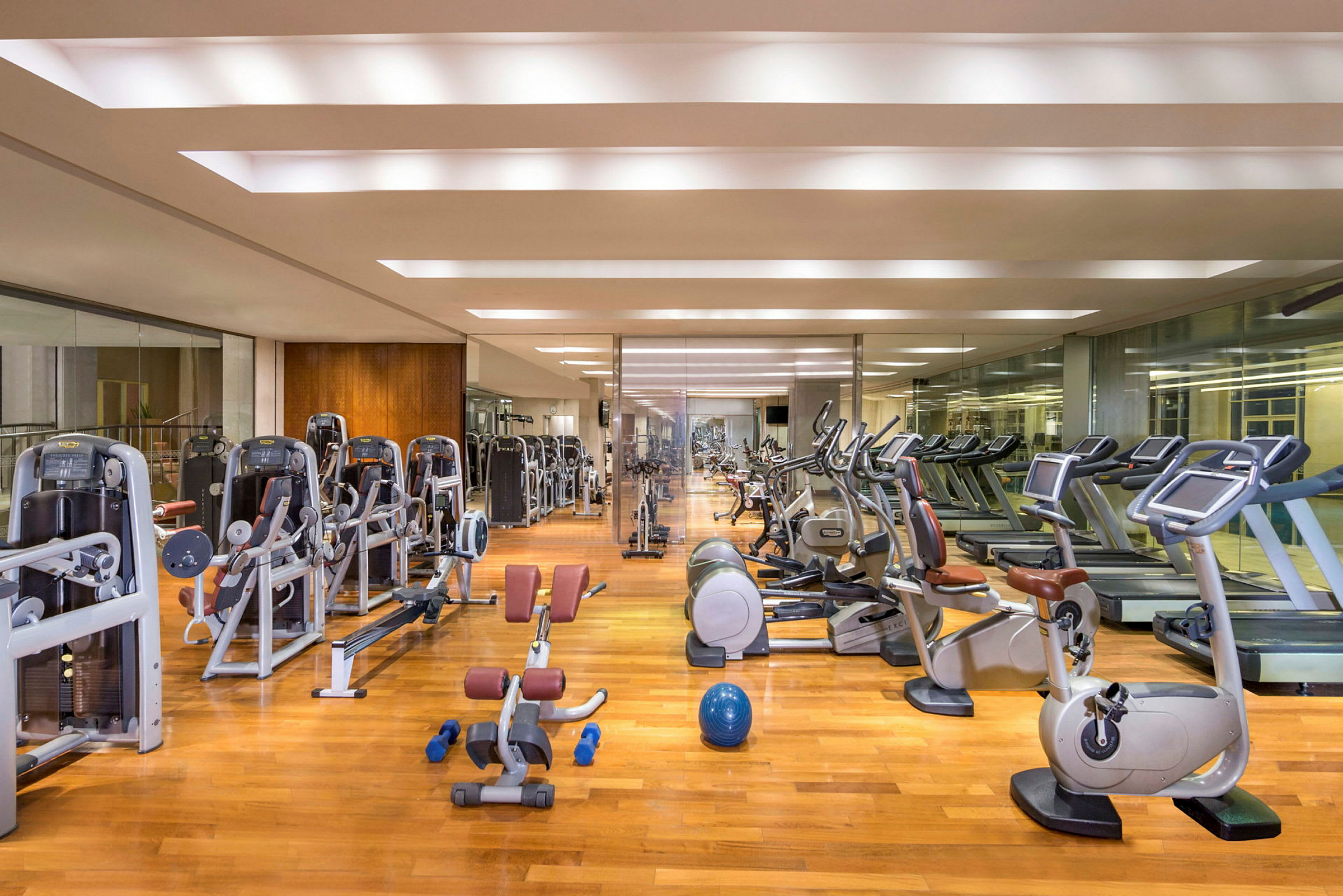Ett gym med träningsmaskiner, löpband, motionscyklar och fria vikter placerade på ett golv av trä. (AI-genererad text)