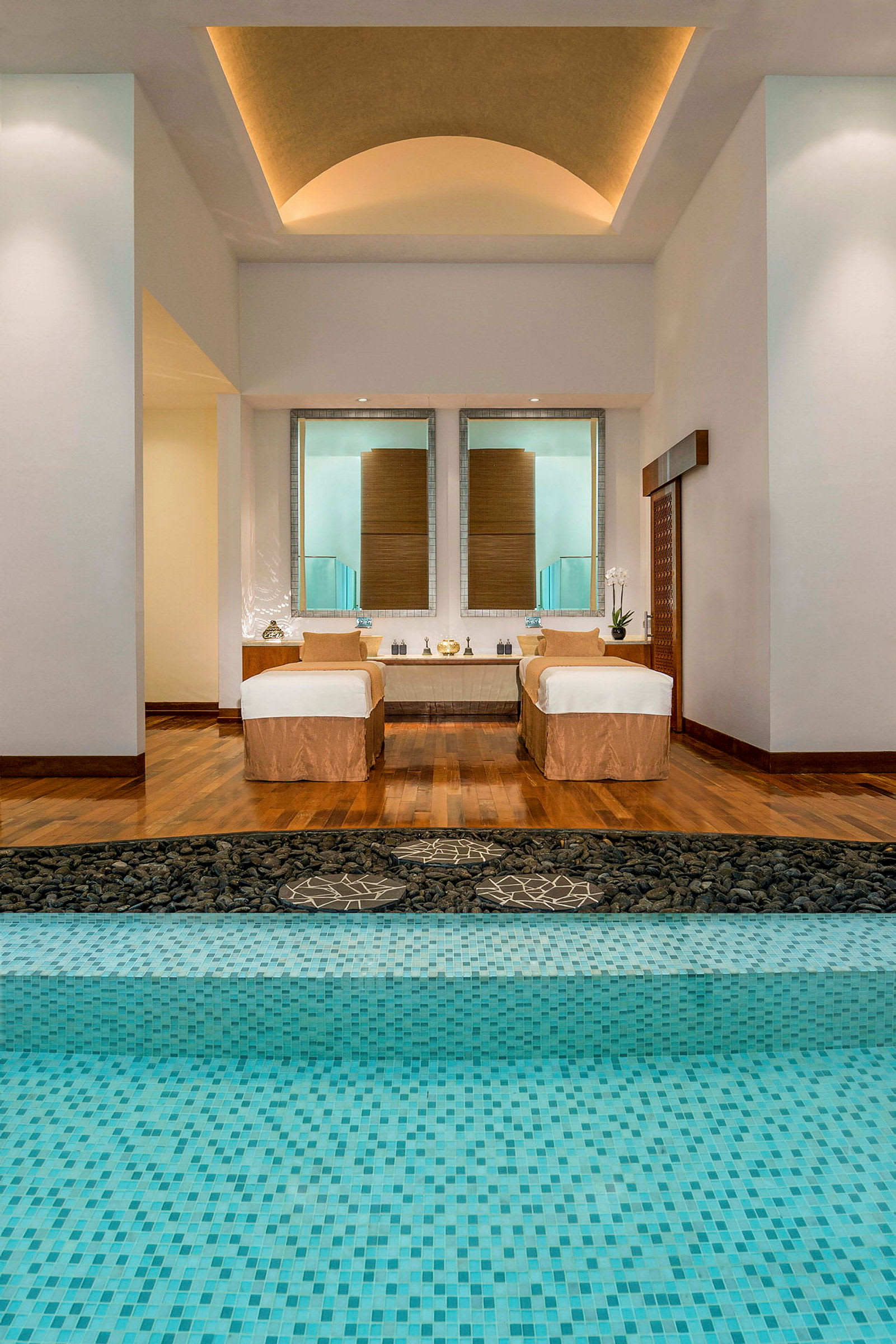 Ett elegant spa med trägolv, två massagebänkar och en pool med turkosa mosaikplattor. (AI-genererad text)