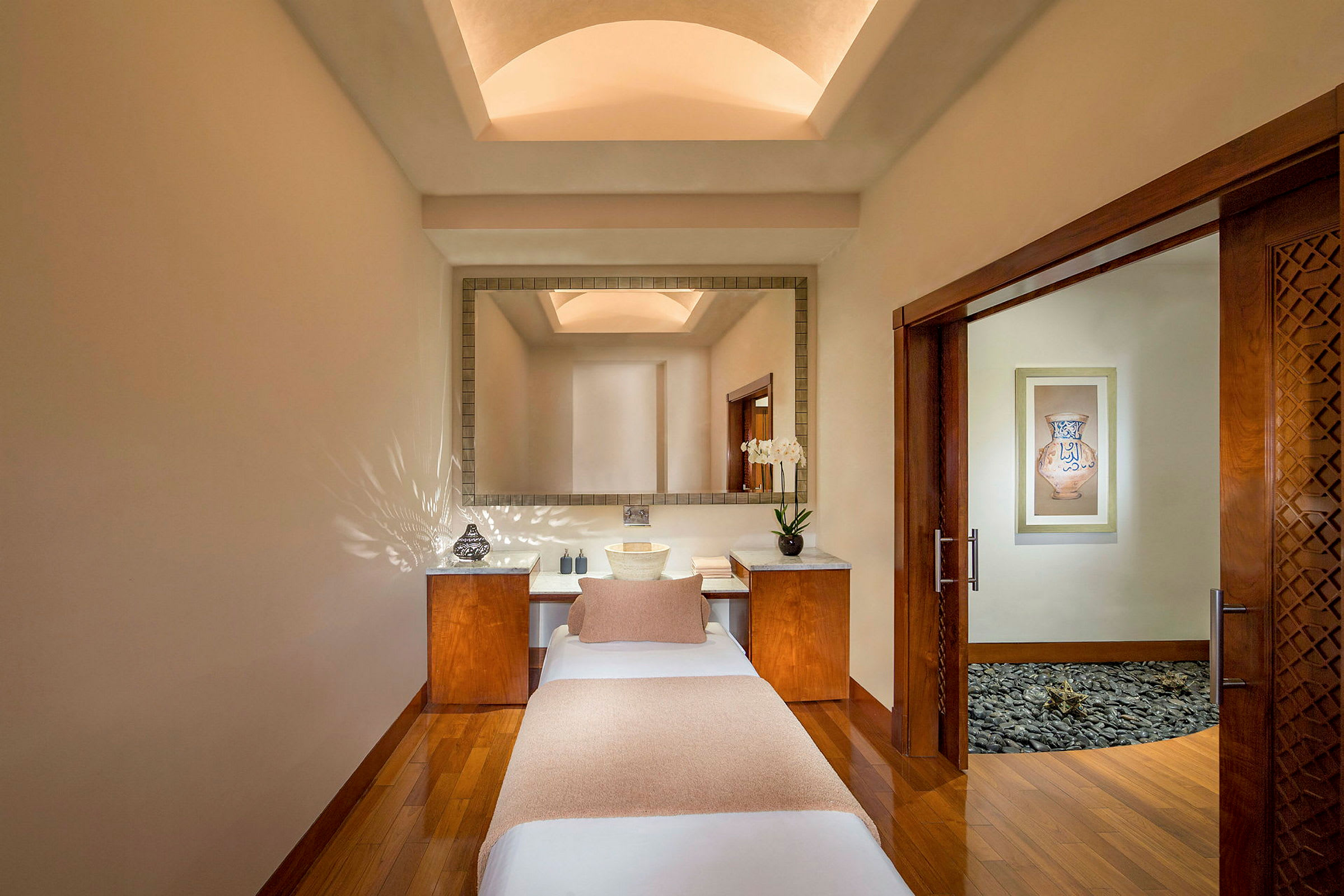 Ett elegant spa-behandlingsrum med en massagebänk, neutrala toner och en dekorativ spegel. (AI-genererad text)