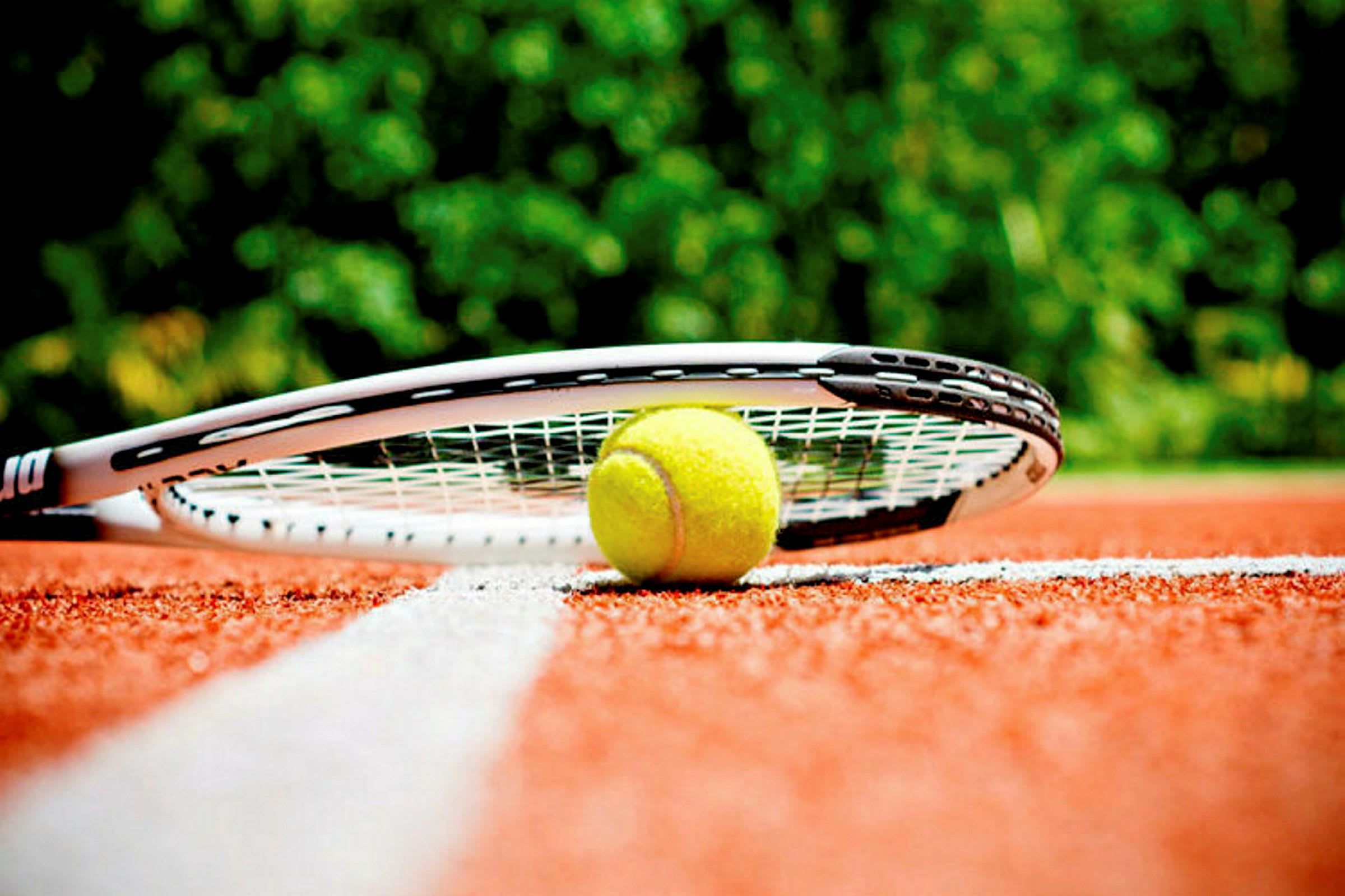 En tennisboll och en racket ligger på en röd tennisbana nära en vit linje. (AI-genererad text)