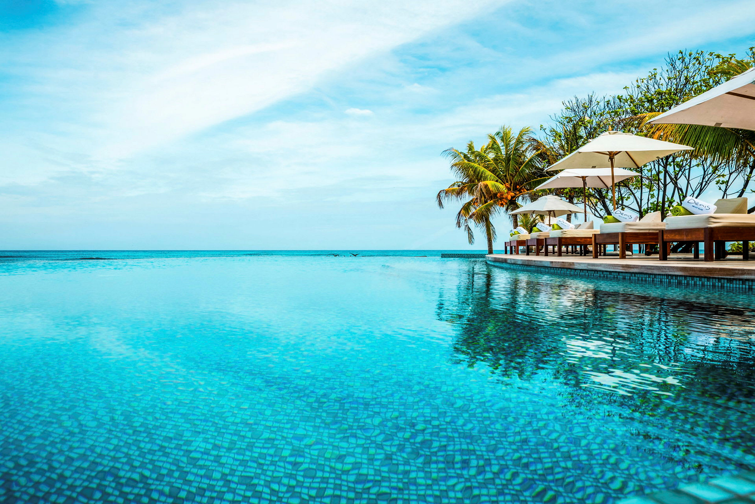 Bild av en infinitypool vid havet med solstolar och parasoller längs kanten. (AI-genererad text)
