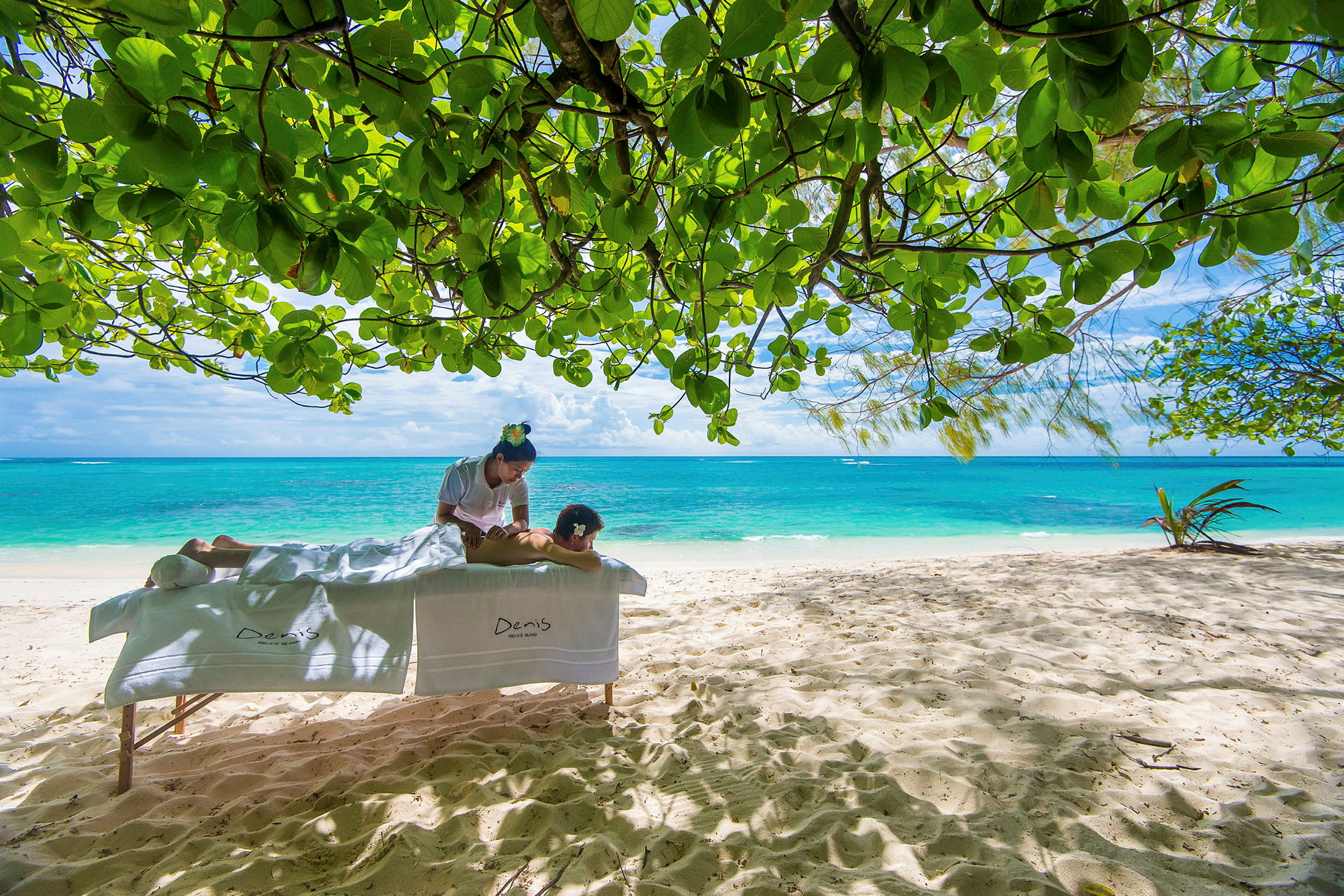 Massage på en sandstrand under gröna träd med utsikt över havet. (AI-genererad text)
