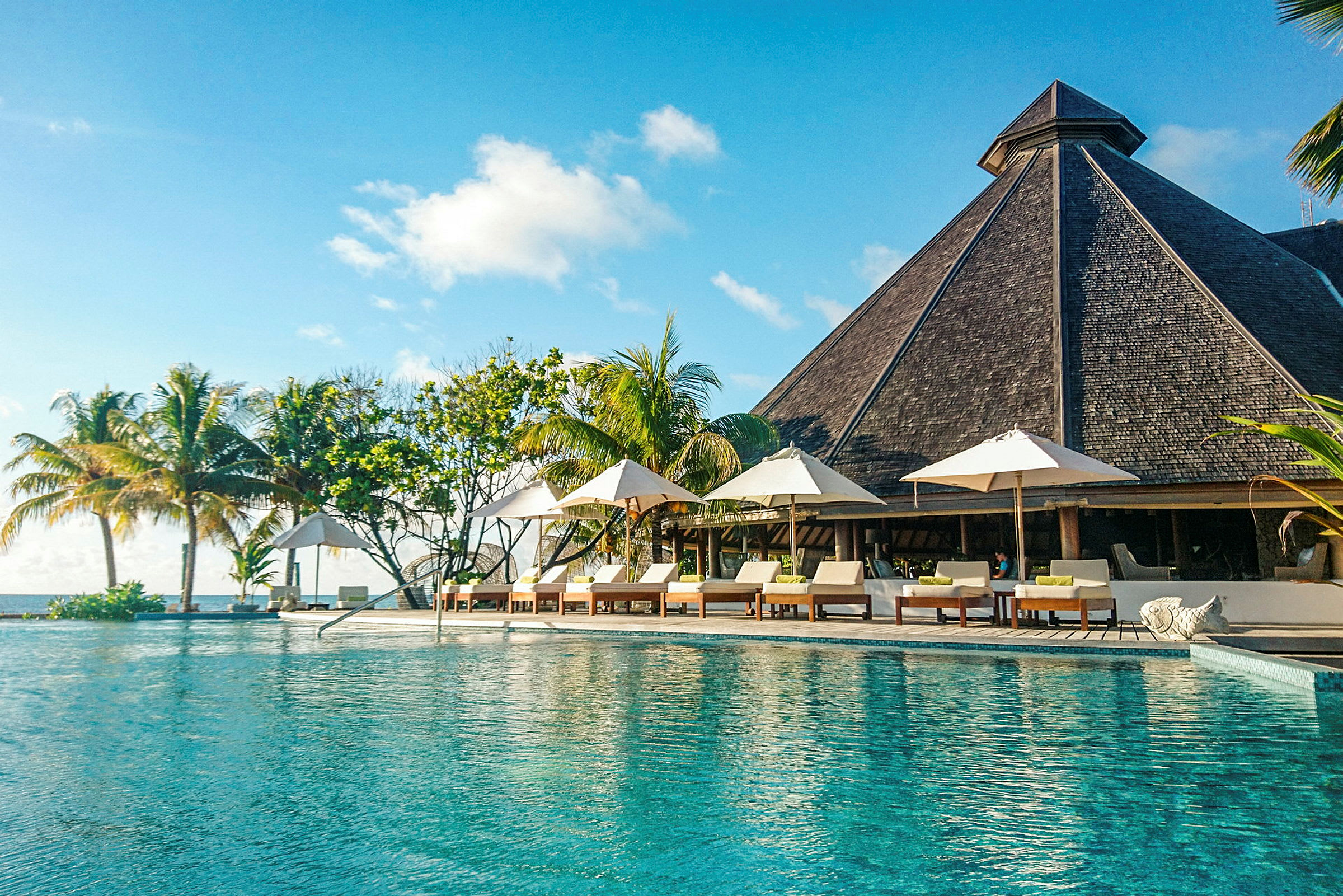 Bild av en pool vid ett semesterhotell med solstolar, parasoller och frodig växtlighet i bakgrunden. (AI-genererad text)