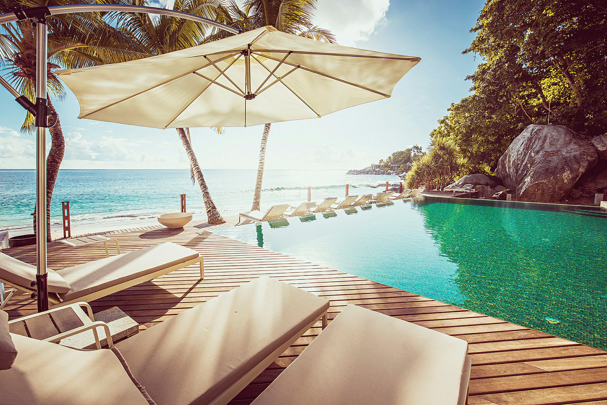 En pool vid stranden med solstolar under parasoller. (AI-genererad text)