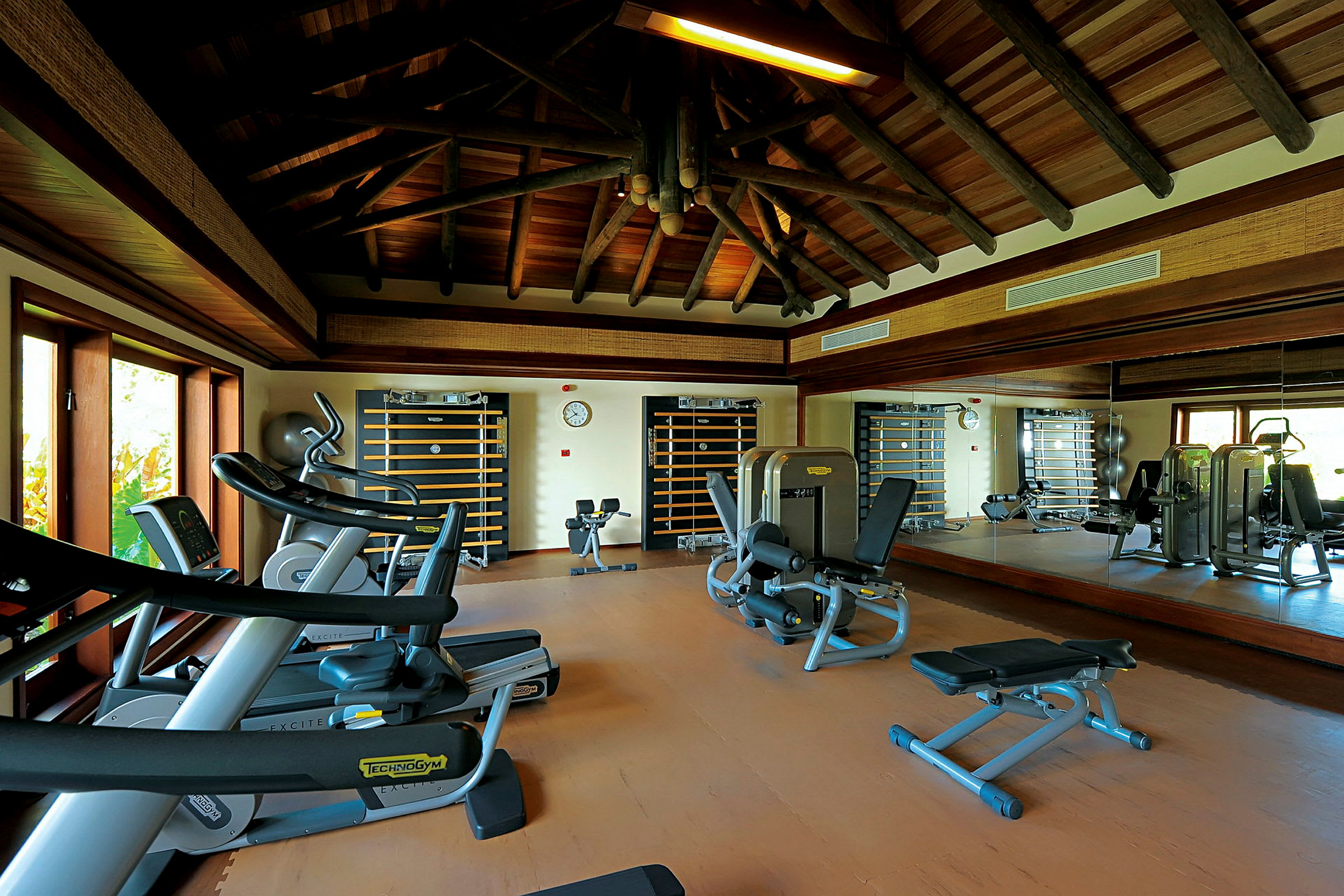 Ett gym med träningsmaskiner, speglar och träbjälkar i taket. (AI-genererad text)