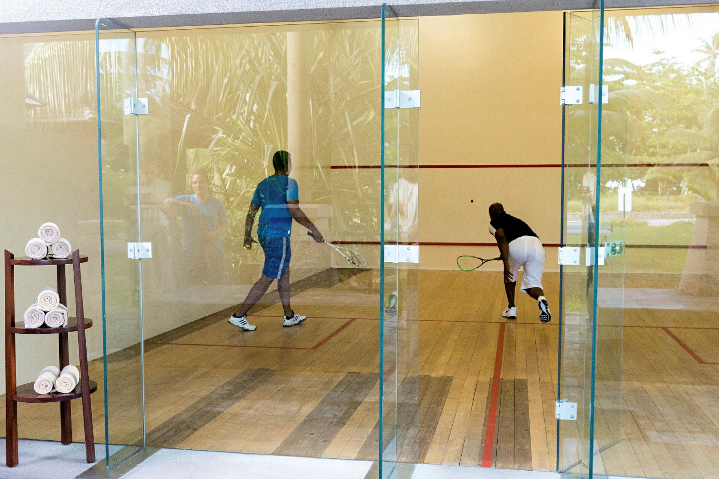 Två personer spelar squash på en bana med glasväggar. (AI-genererad text)