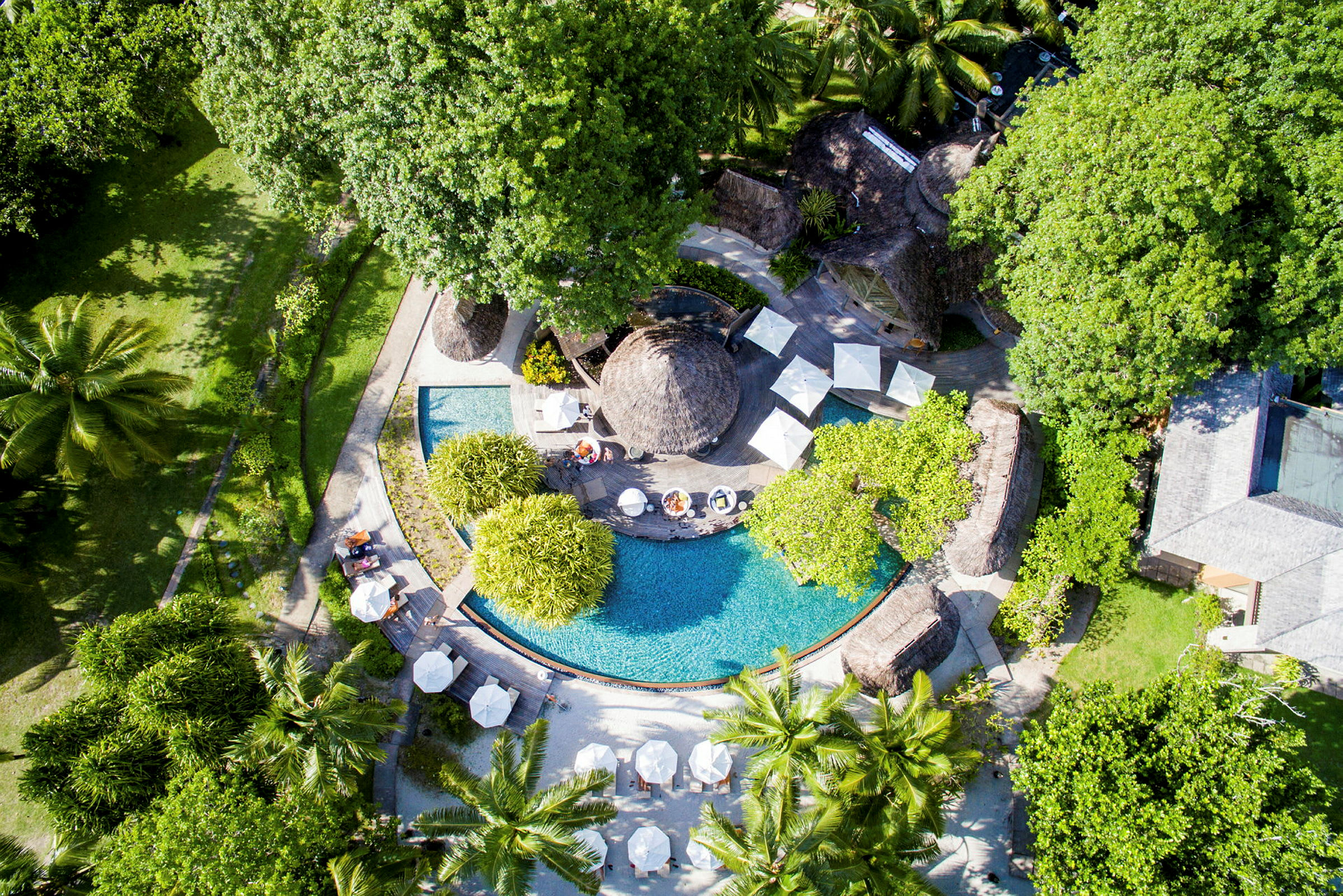 Flygfoto av ett under palmskydd omgiven semesterort med pool och parasoller. (AI-genererad text)