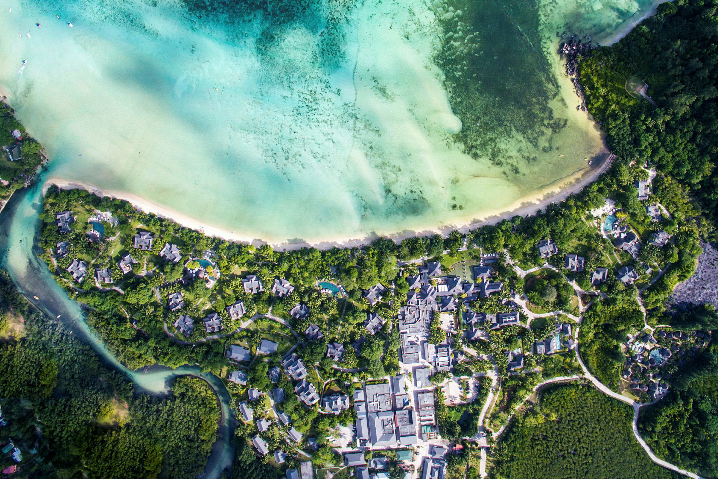 Flygfoto av en kust med grönt vatten, vita stränder och omgivande bebyggelse. (AI-genererad text)