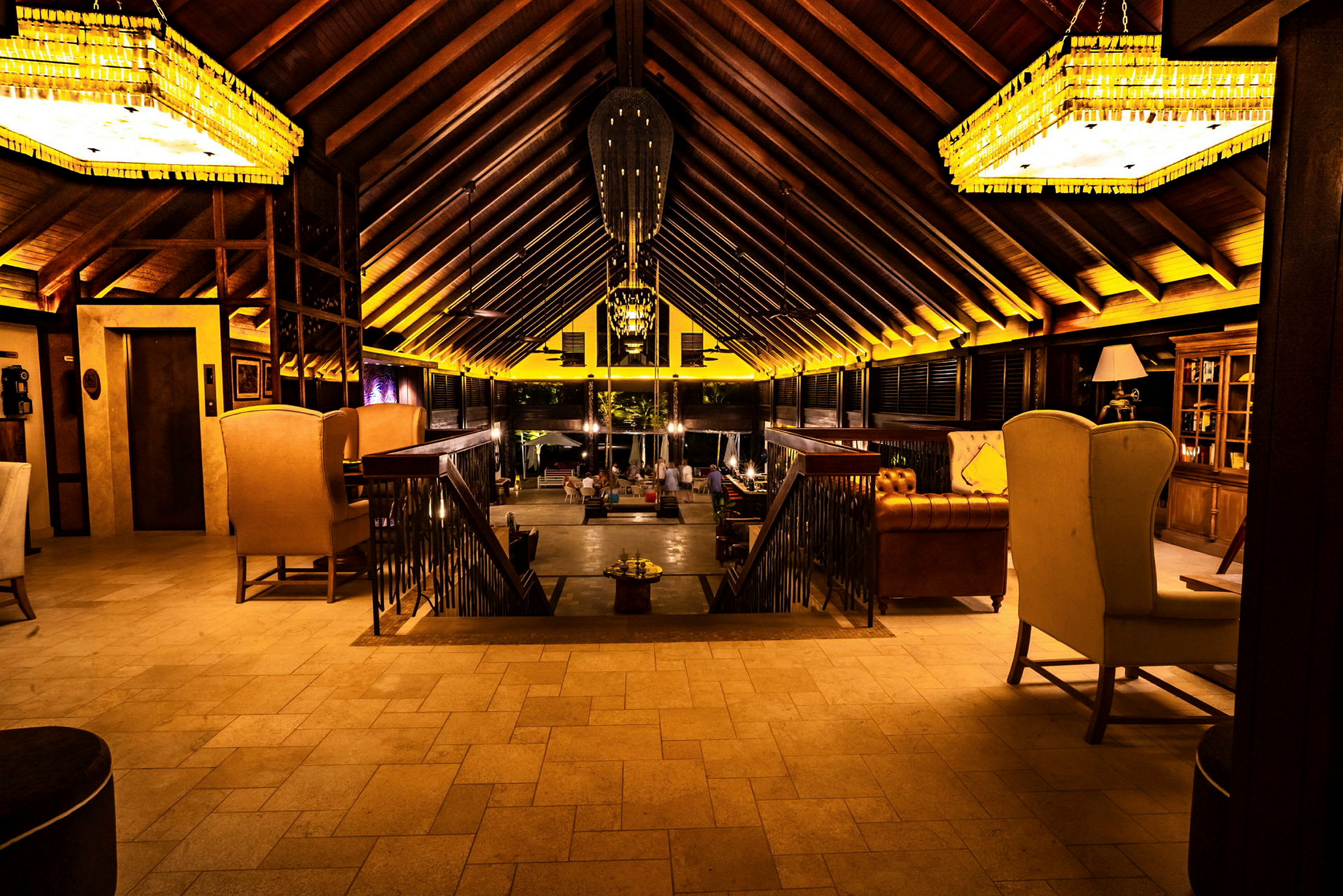 Interiör av en lodge med högt tak, sittmöbler och en trappa som leder ner till en lounge-område. (AI-genererad text)