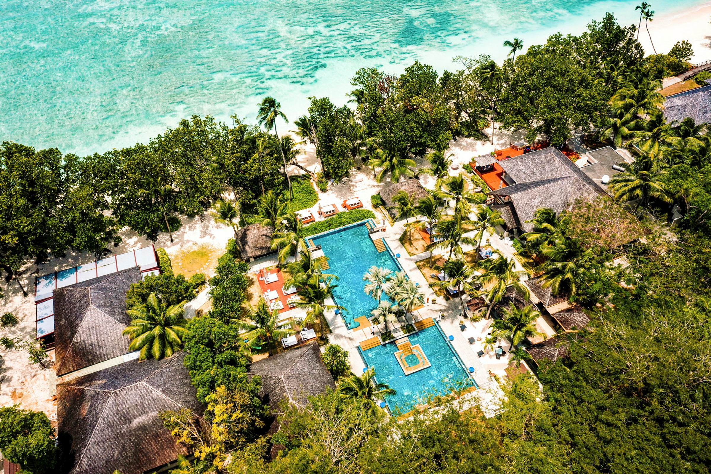 Flygfoto över en resort med en pool, omgiven av palmer och nära havet. (AI-genererad text)