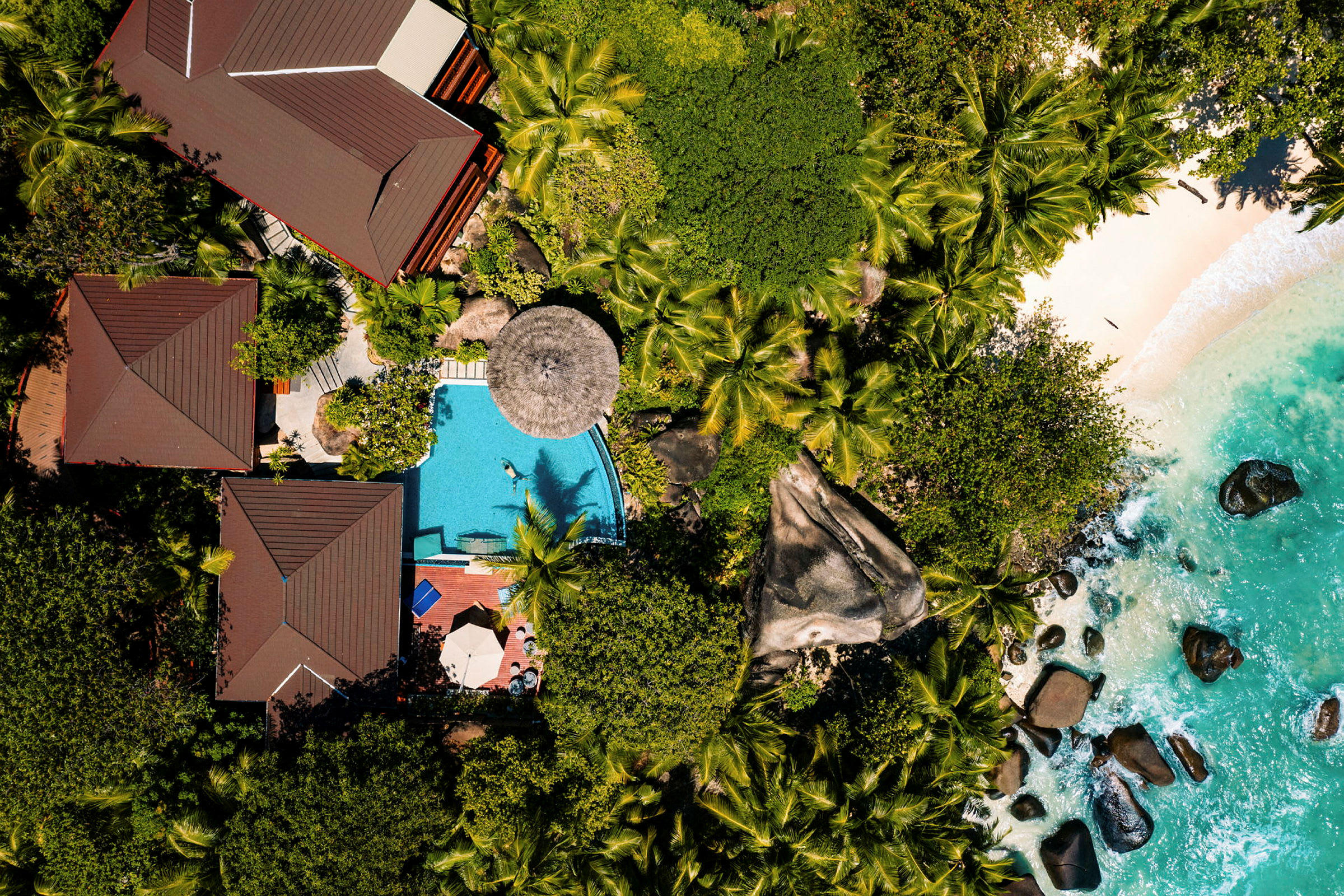 Flygfoto över tropisk resort med pool, strand, och grönska. (AI-genererad text)