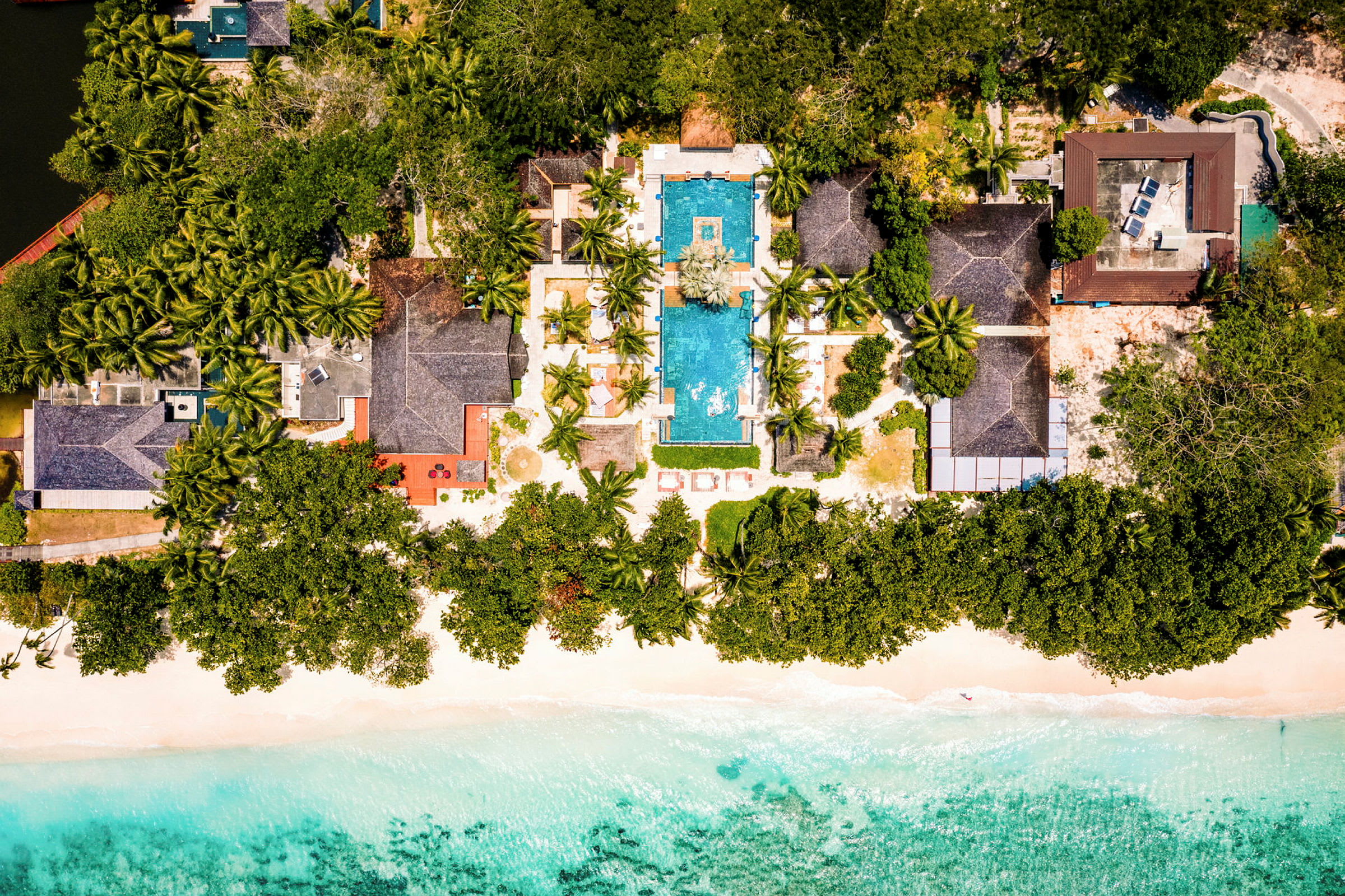 Flygfoto av en resort med pool och omgivande grönska vid en strand. (AI-genererad text)