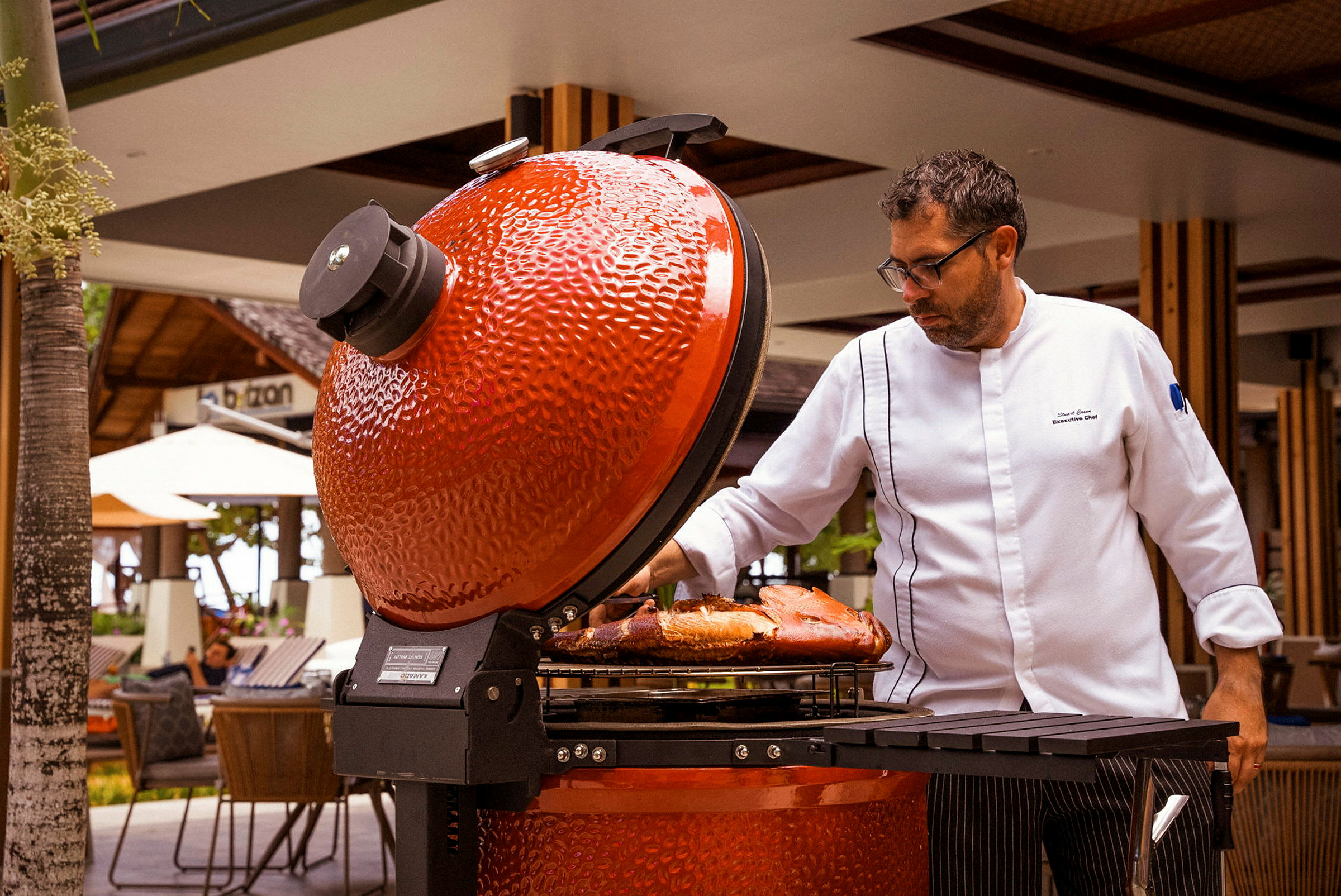 Person vid öppnad röd grill med mat på gallret. (AI-genererad text)