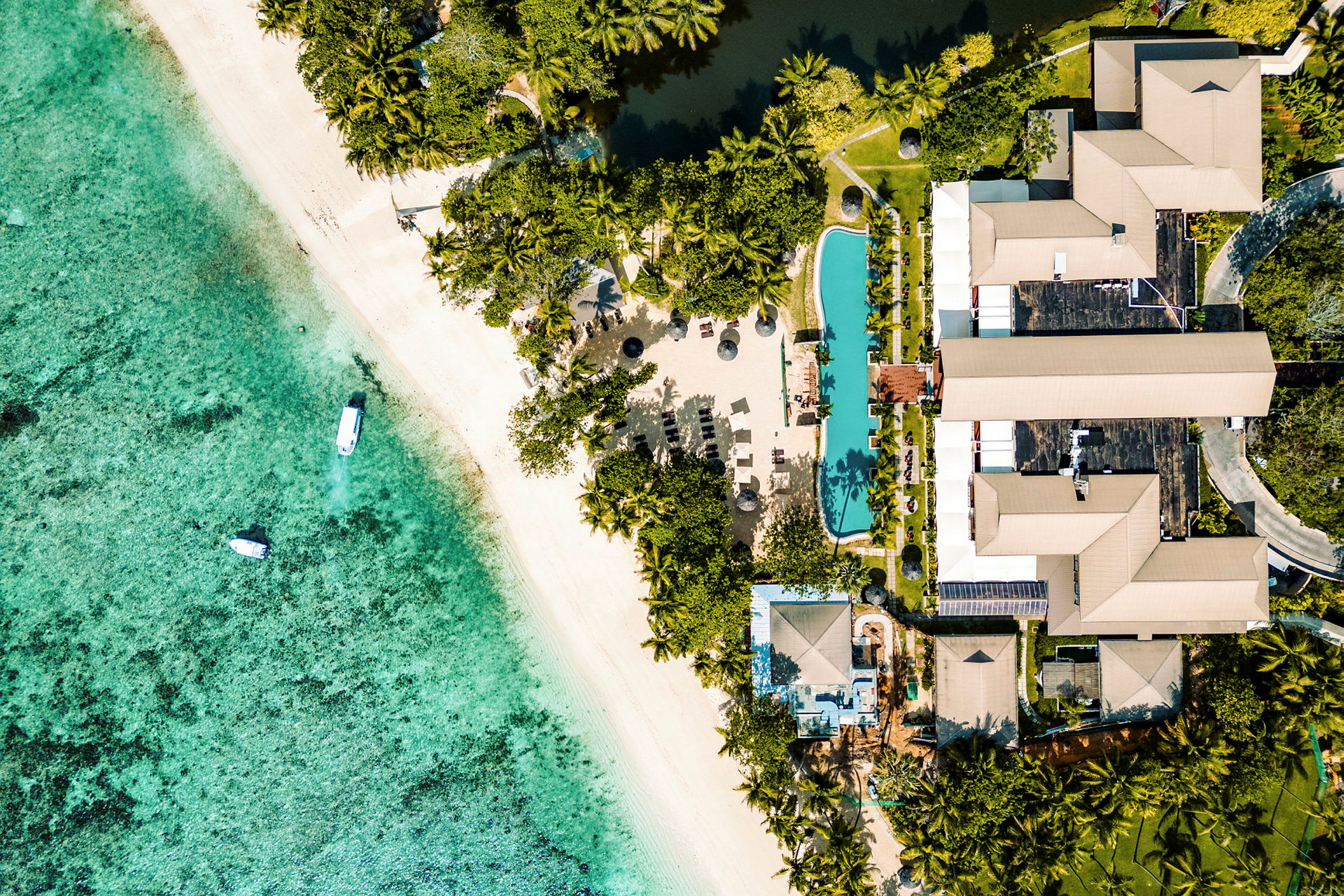 Flygbild över en strand och resort med palmträd, pool och byggnader. (AI-genererad text)