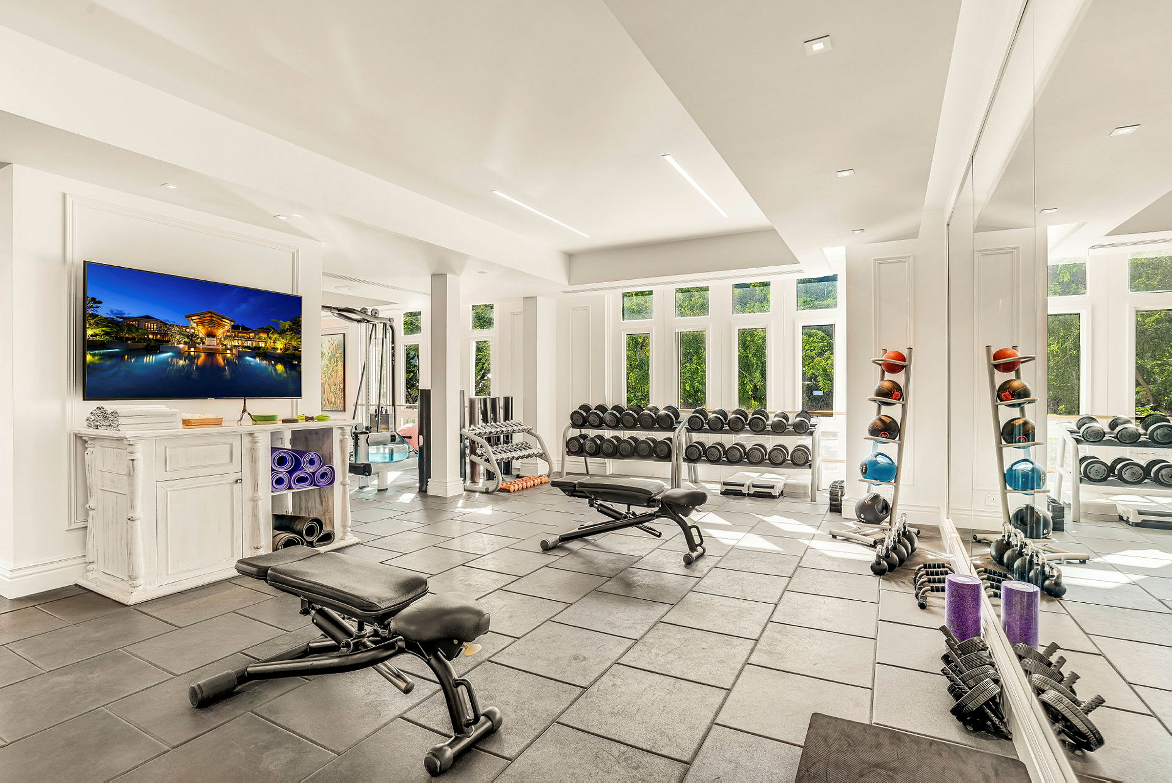 Ett gym med träningsutrustning som hantlar, träningsbänkar och yogamattor, med ett stort fönster som släpper in naturligt ljus. (AI-genererad text)