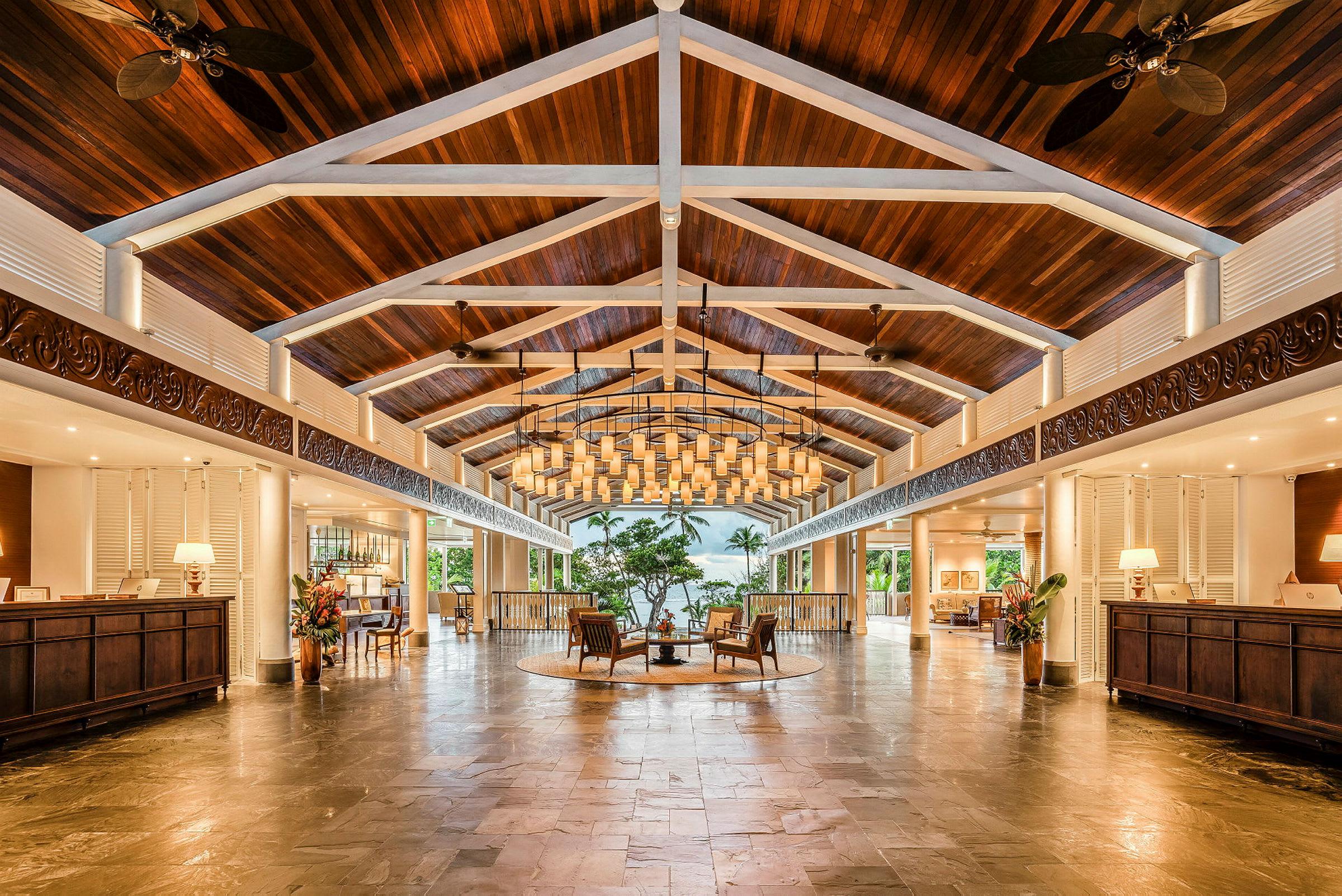 Ett hotellobby med högt tak av träbjälkar och snygg belysning, möbler i mitten och receptioner på sidorna. (AI-genererad text)