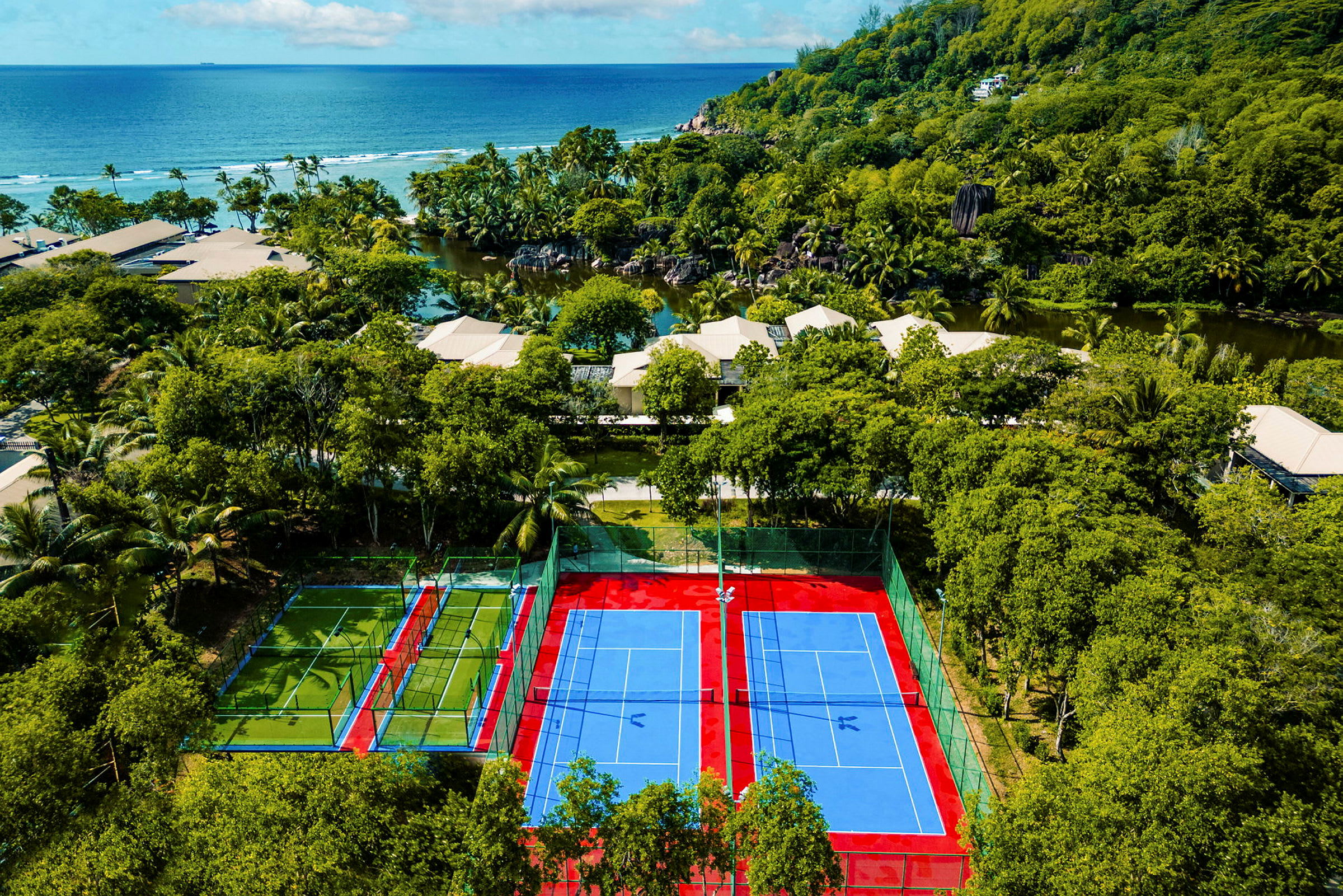 Två tennisbanor omgivna av grönska, med havet synligt i bakgrunden. (AI-genererad text)