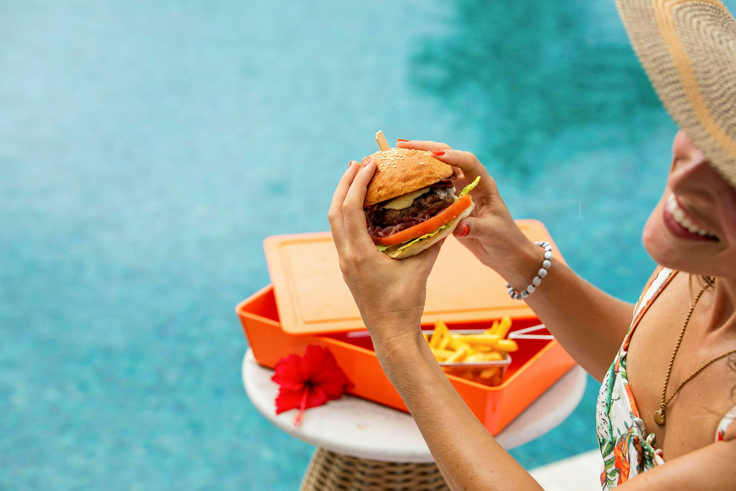 En person håller i en hamburgare vid ett bord nära en pool. (AI-genererad text)