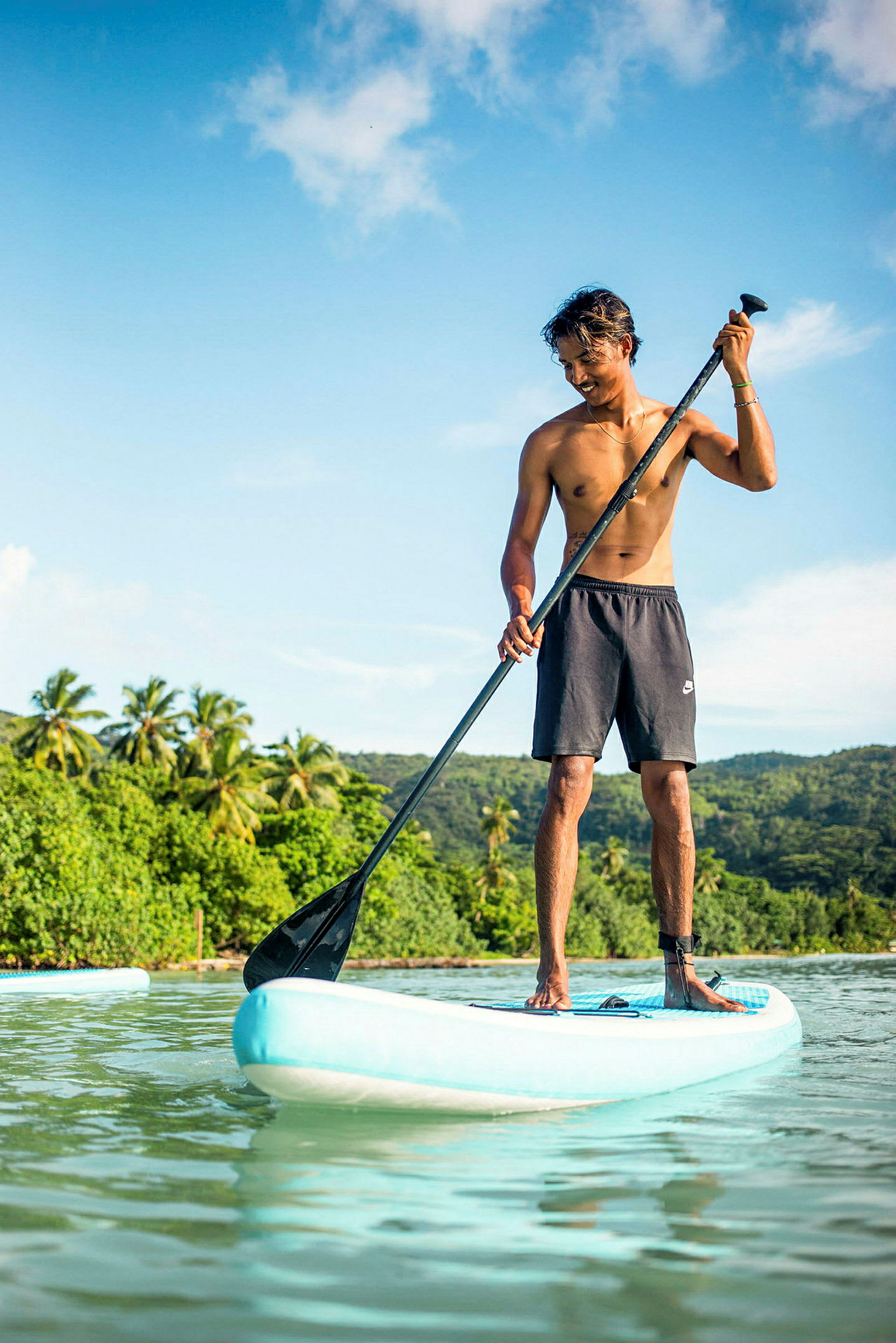 En person står på en paddleboard och paddlar i en lugn vattenmiljö med grönskande träd i bakgrunden. (AI-genererad text)
