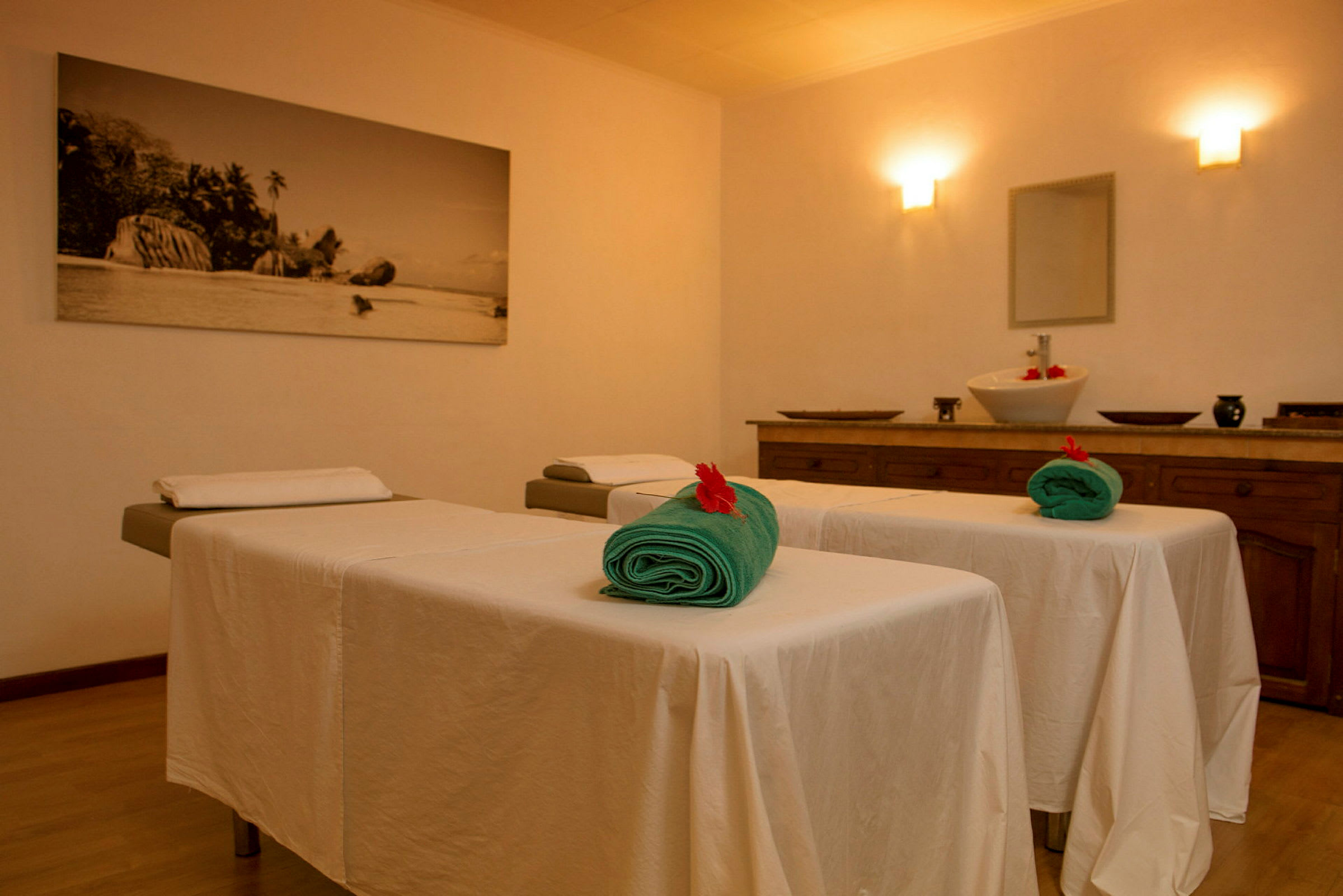Interiör av ett spa med två massagebord klädda med vita dukar och gröna handdukar. I bakgrunden syns ett bord med en skål. (AI-genererad text)