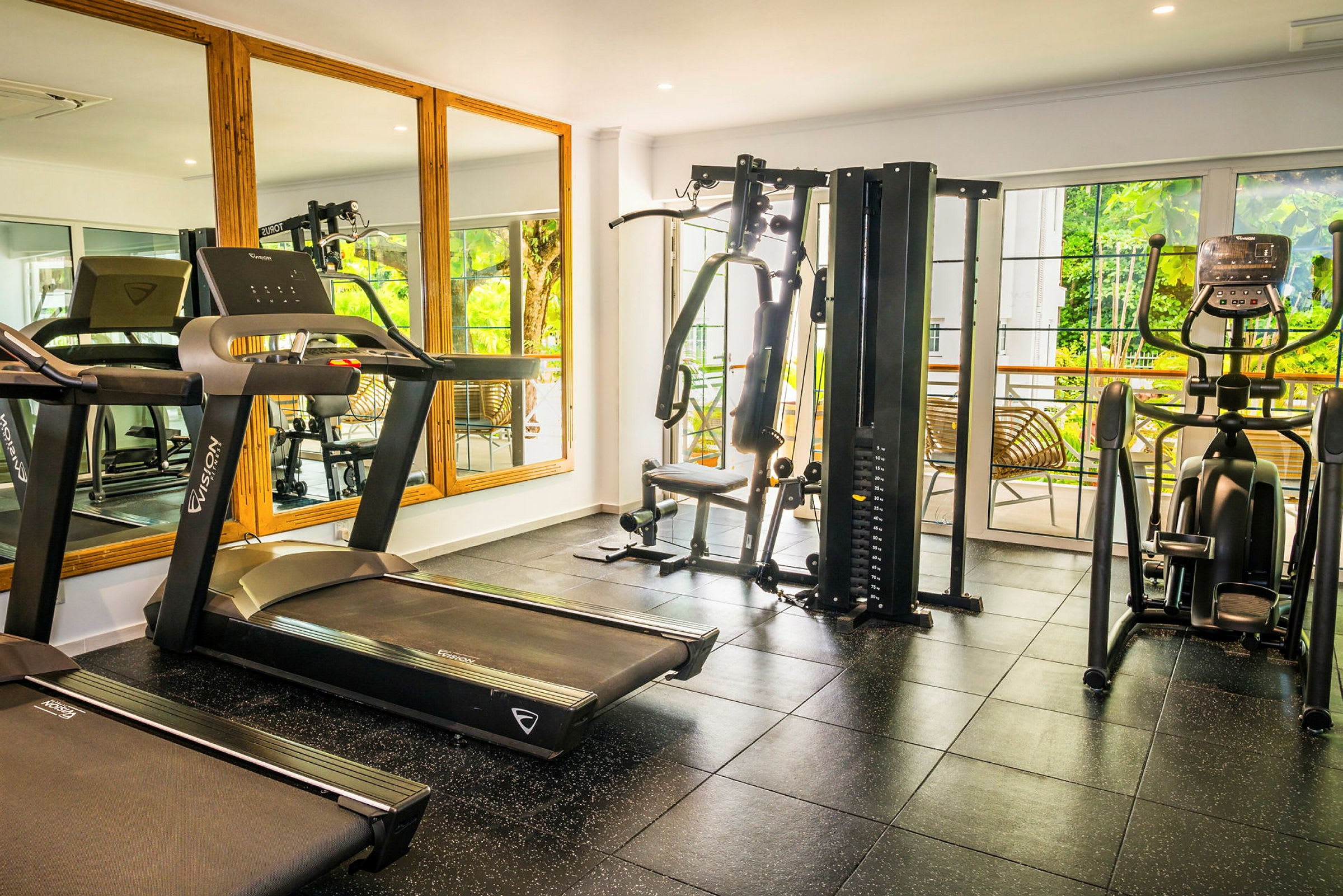 Ett gym med olika träningsmaskiner, inklusive löpband, multigym och träningscykel. Bakom träningsmaskinerna finns stora fönster och speglar. (AI-genererad text)
