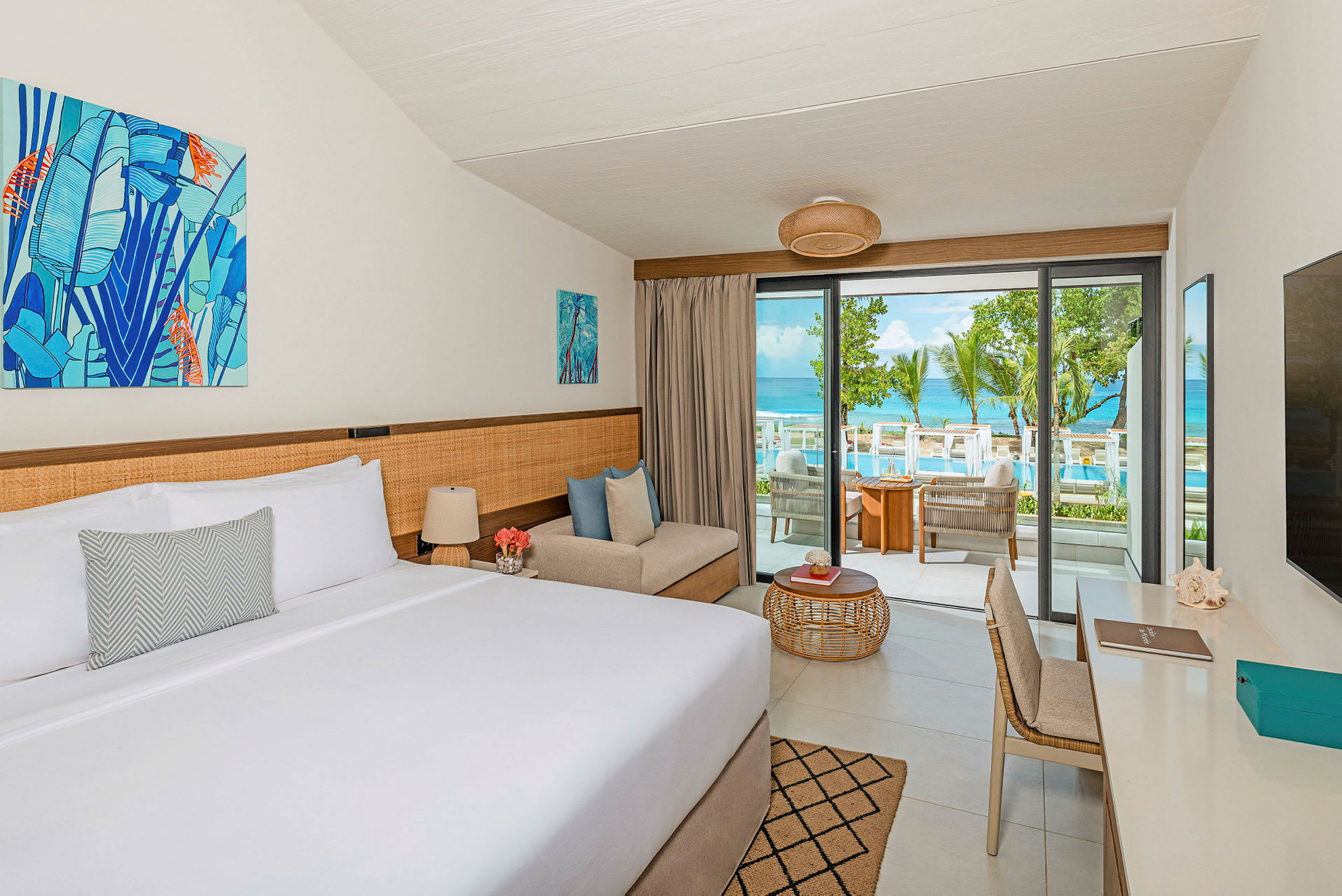 Ett hotellrum med en dubbelsäng, en sittplats och en balkong med utsikt över en pool och havet. (AI-genererad text)