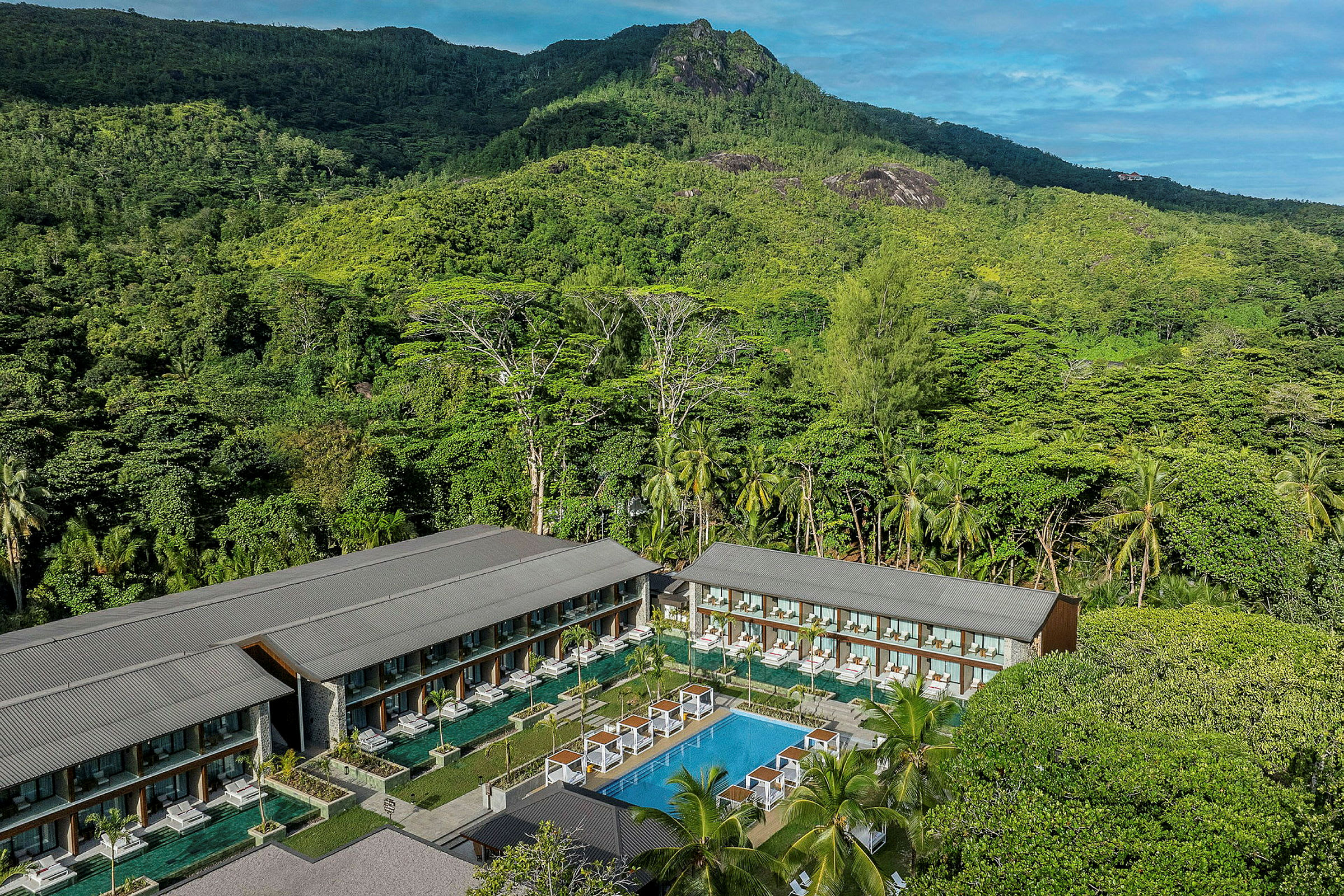 Bild av en resort omgiven av frodig grönska och höga berg med en pool i mitten. (AI-genererad text)