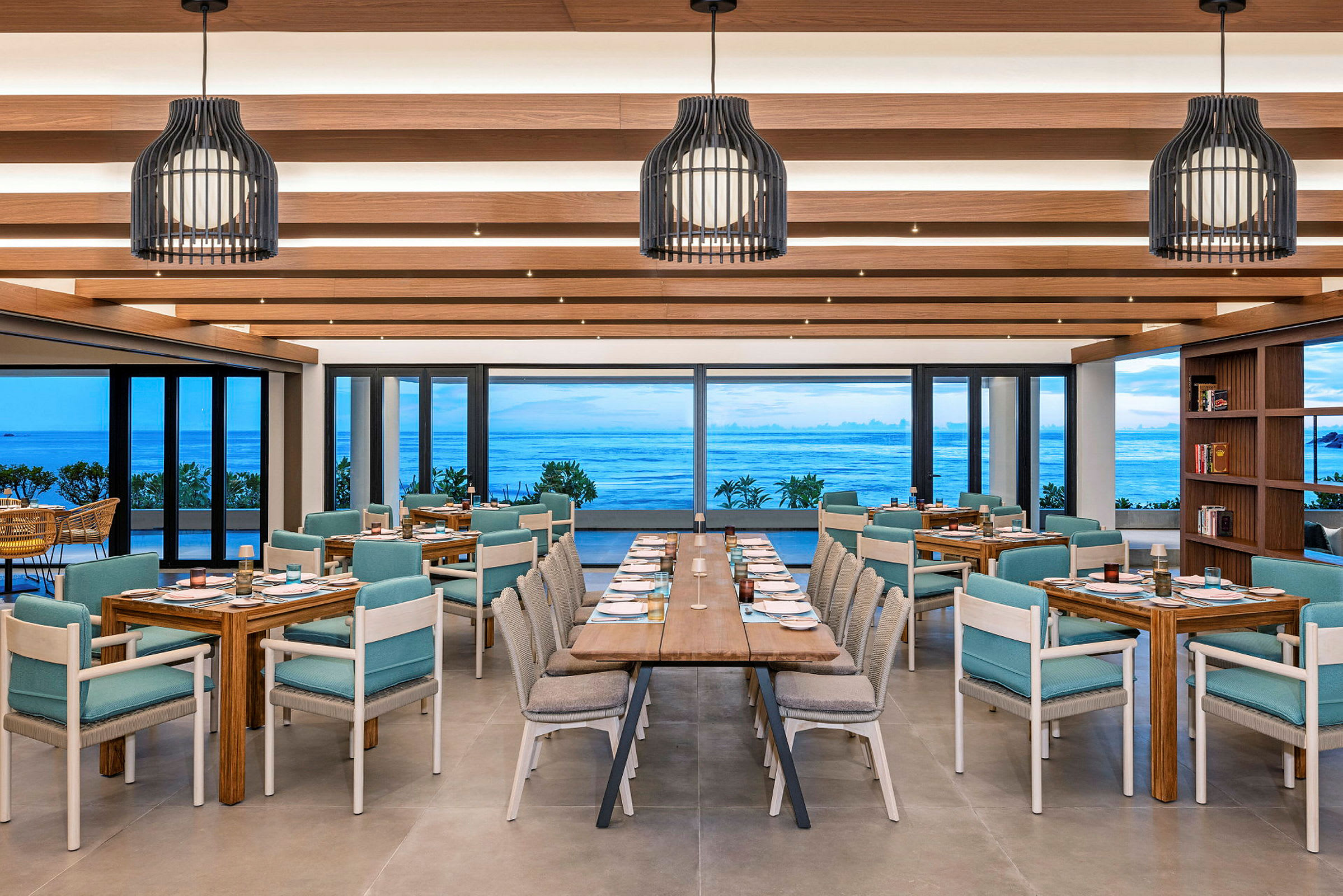 En restaurang med utsikt över havet genom stora fönster. Lokalen har trädetaljer, moderna möbler och dukade bord. (AI-genererad text)