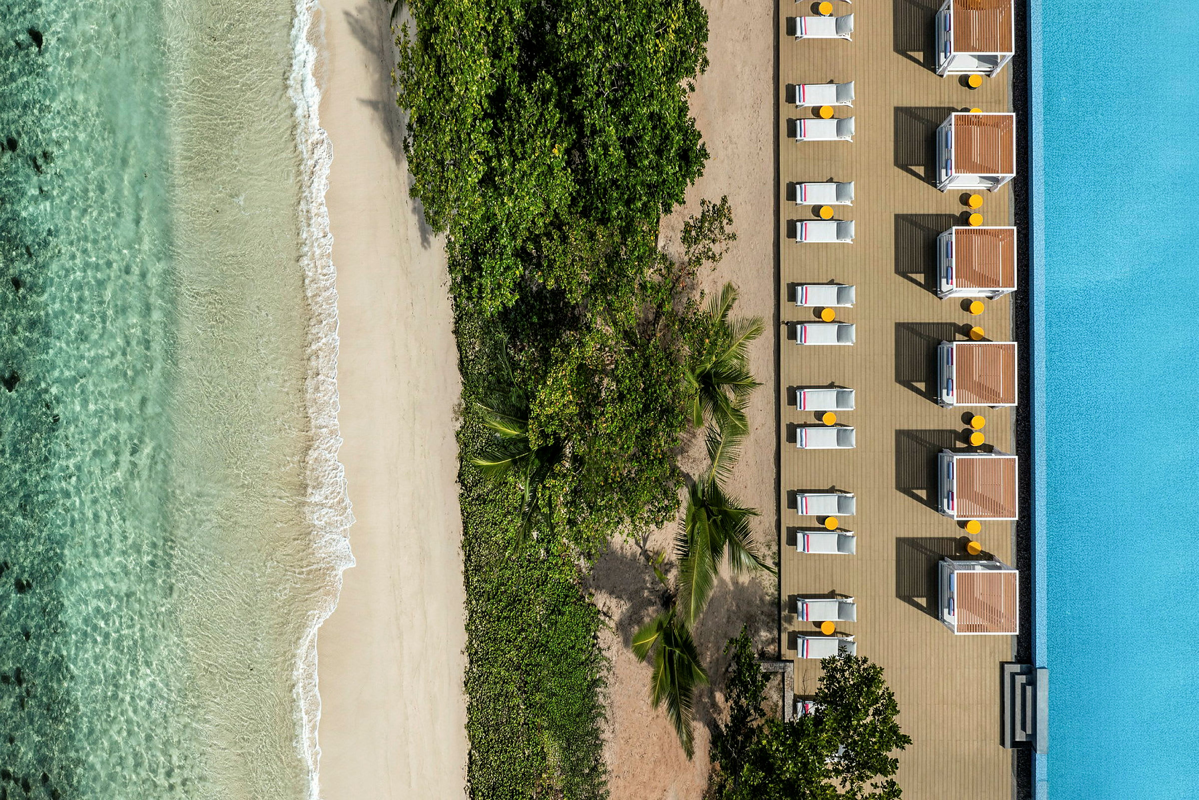 Flygfoto av strand med klart vatten, grönska och solstolar vid en pool. (AI-genererad text)