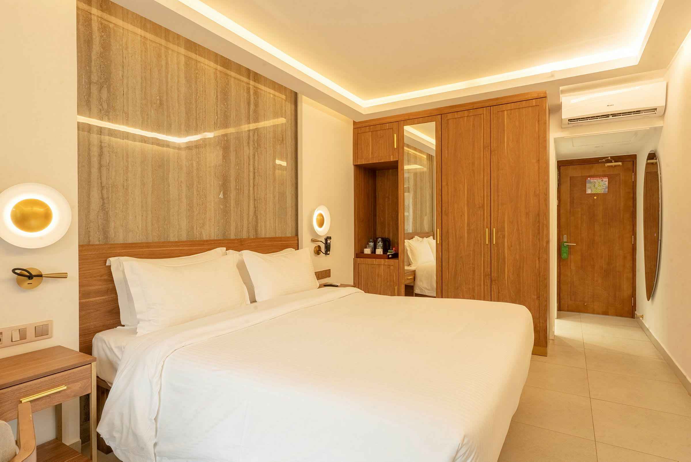 Ett hotellrum med en stor säng täckt med vita lakan, träpaneler på väggen bakom och träinredning inklusive en garderob och ett skrivbord. (AI-genererad text)