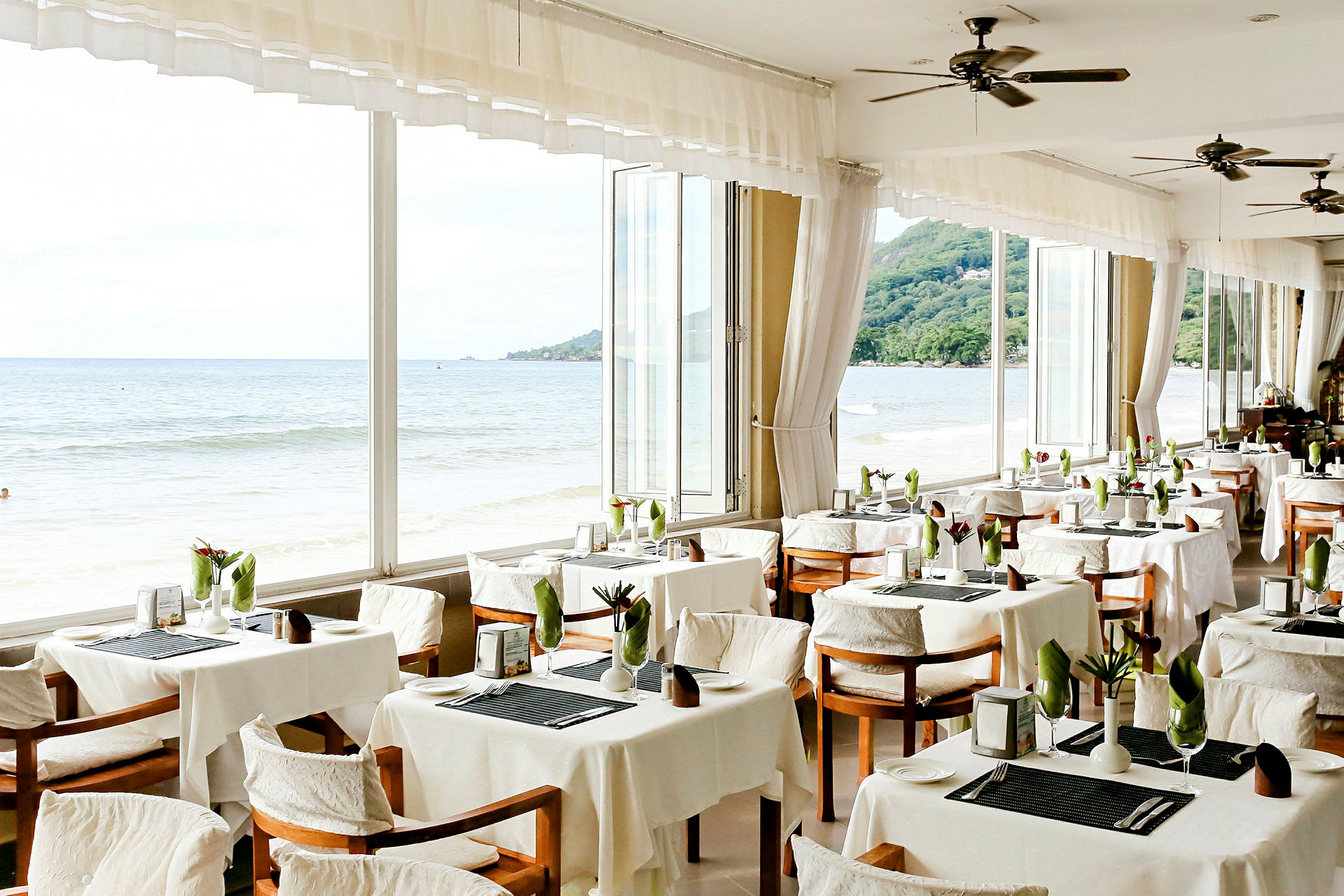 Restaurang med dukade bord och utsikt över havet genom stora fönster. (AI-genererad text)