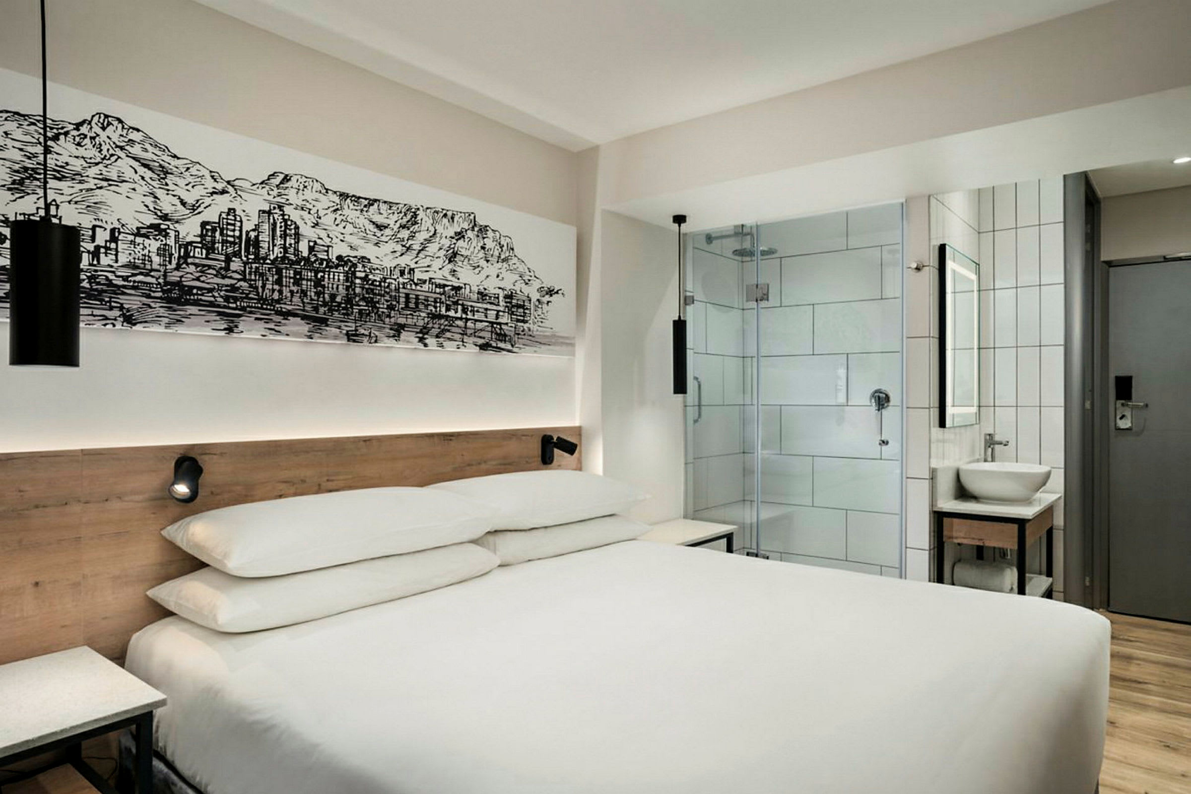 Modernt hotellrum med en dubbelsäng, glasdörr till badrummet och väggkonst. (AI-genererad text)