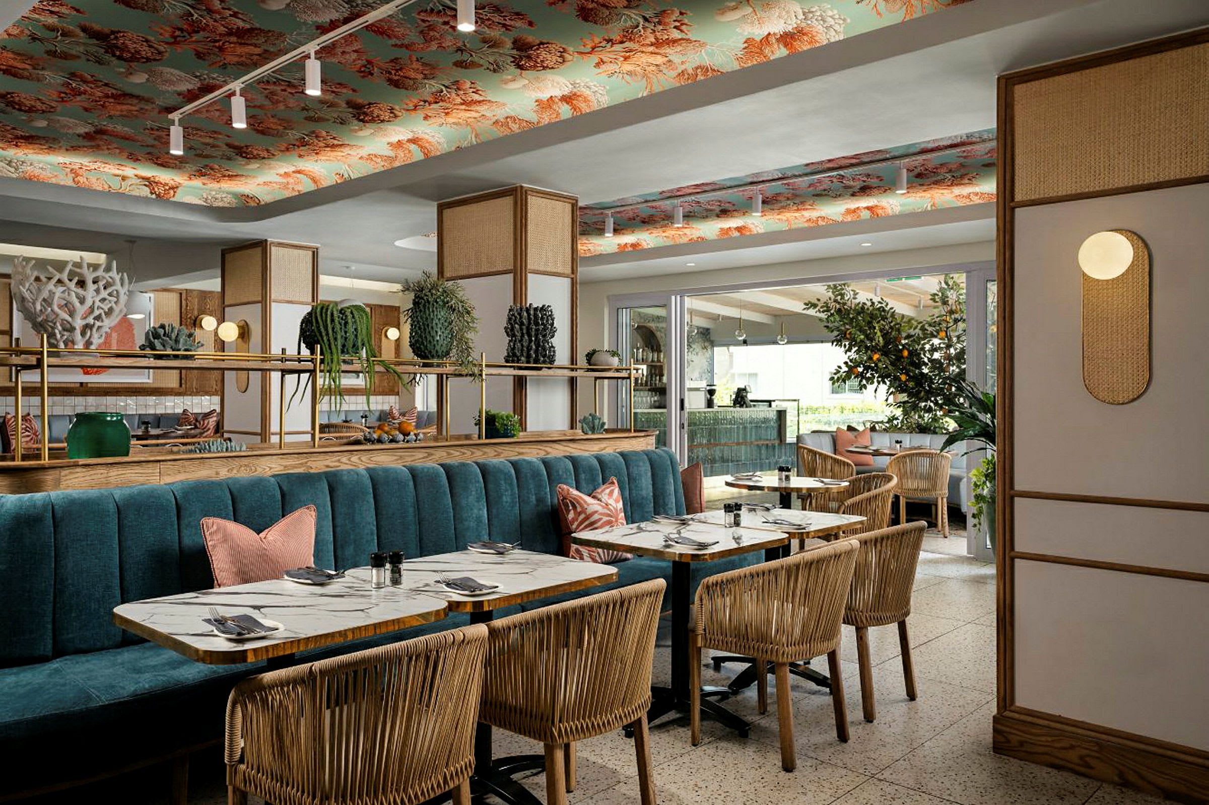 Ett elegant restauranginteriör med trästolar, marmorbord, och en blå soffbänk. Taket är dekorerat med mönster, och inredningen är kompletterad med växter och belysning. (AI-genererad text)