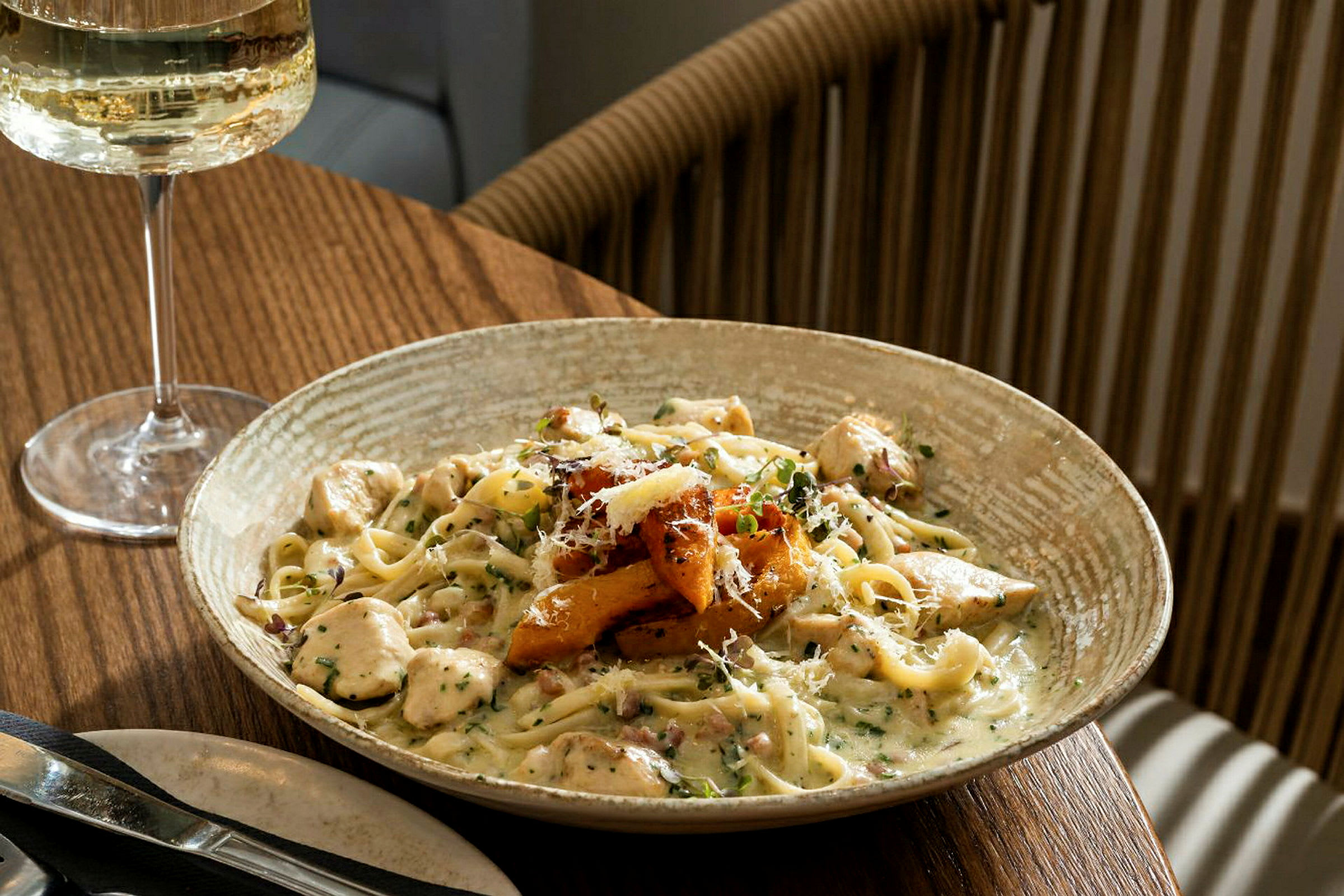 En tallrik pasta med krämig sås och tillbehör, serverad på ett matbord med ett glas vitt vin. (AI-genererad text)