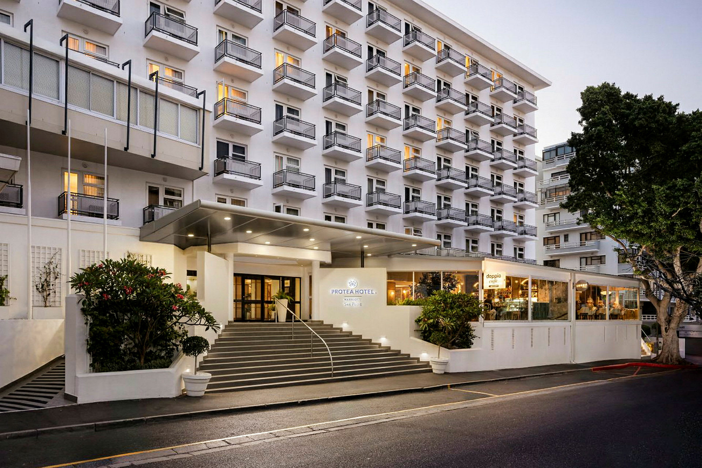 Hotellbyggnad med flera våningar och balkonger, samt en upplyst entré och trappa framför. (AI-genererad text)