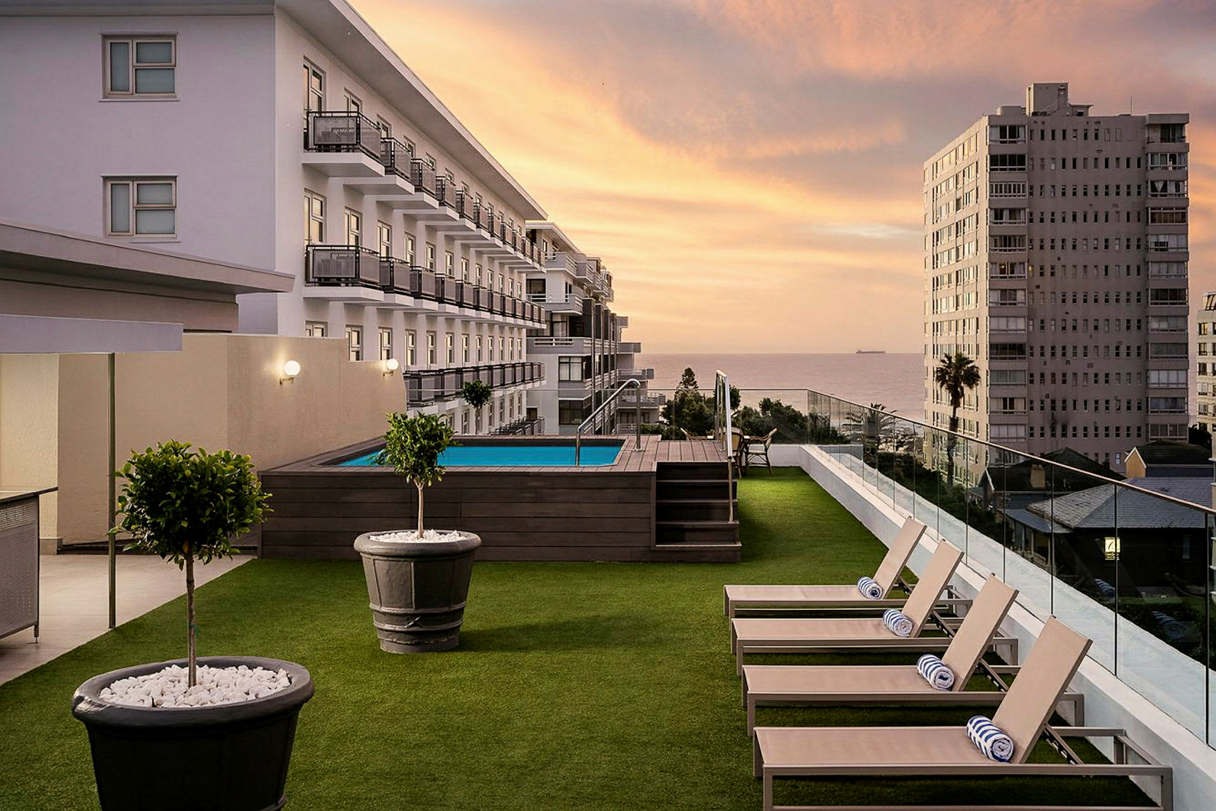 Ett hotellområde med en gräsyta och solstolar vid en pool i solnedgången. (AI-genererad text)