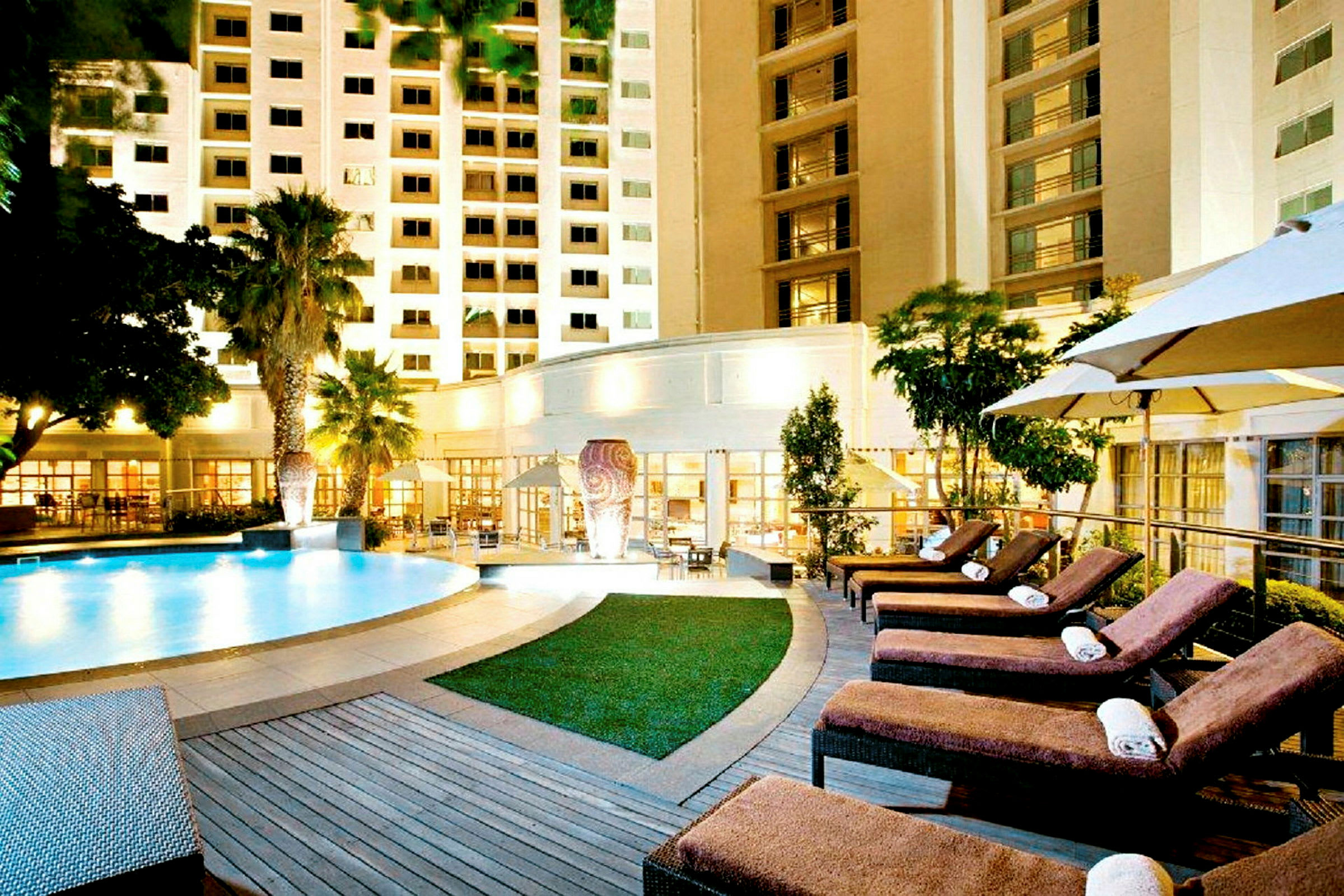 Hotell med upplyst pool och solstolar. (AI-genererad text)