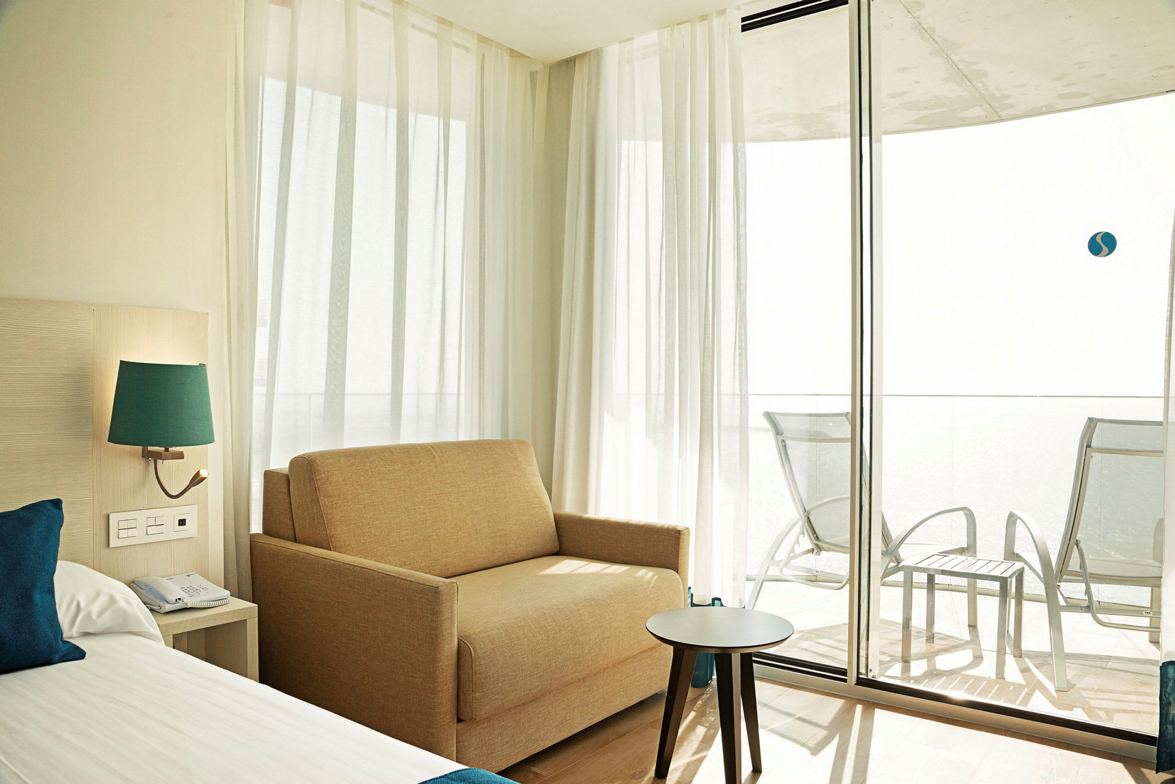 Ett hotellrum med en bädd, en soffa och ett bord nära glasdörrar som leder till en möblerad balkong. (AI-genererad text)