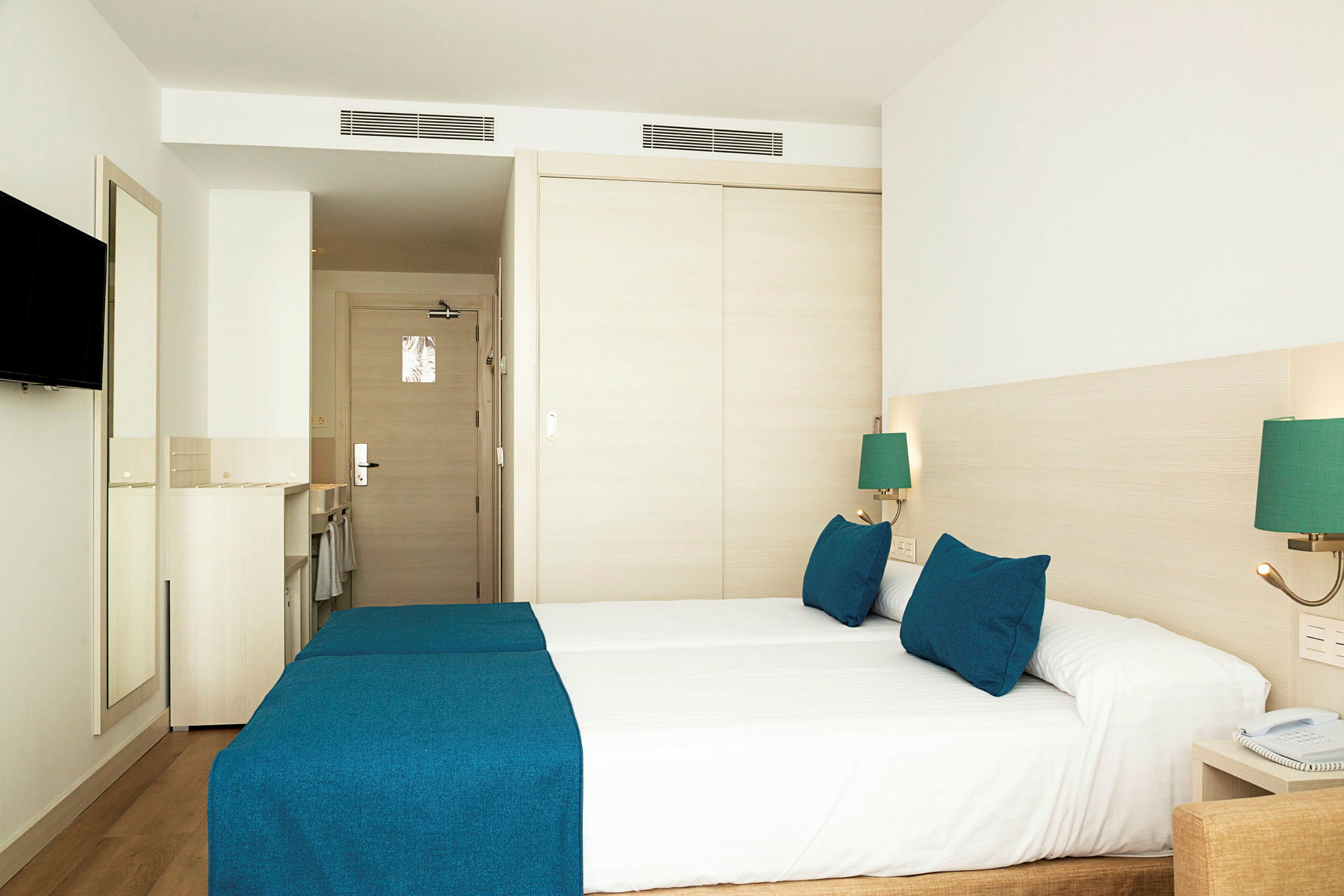 Hotellrum med två bäddar täckta med blå överkast och matchande kuddar. (AI-genererad text)