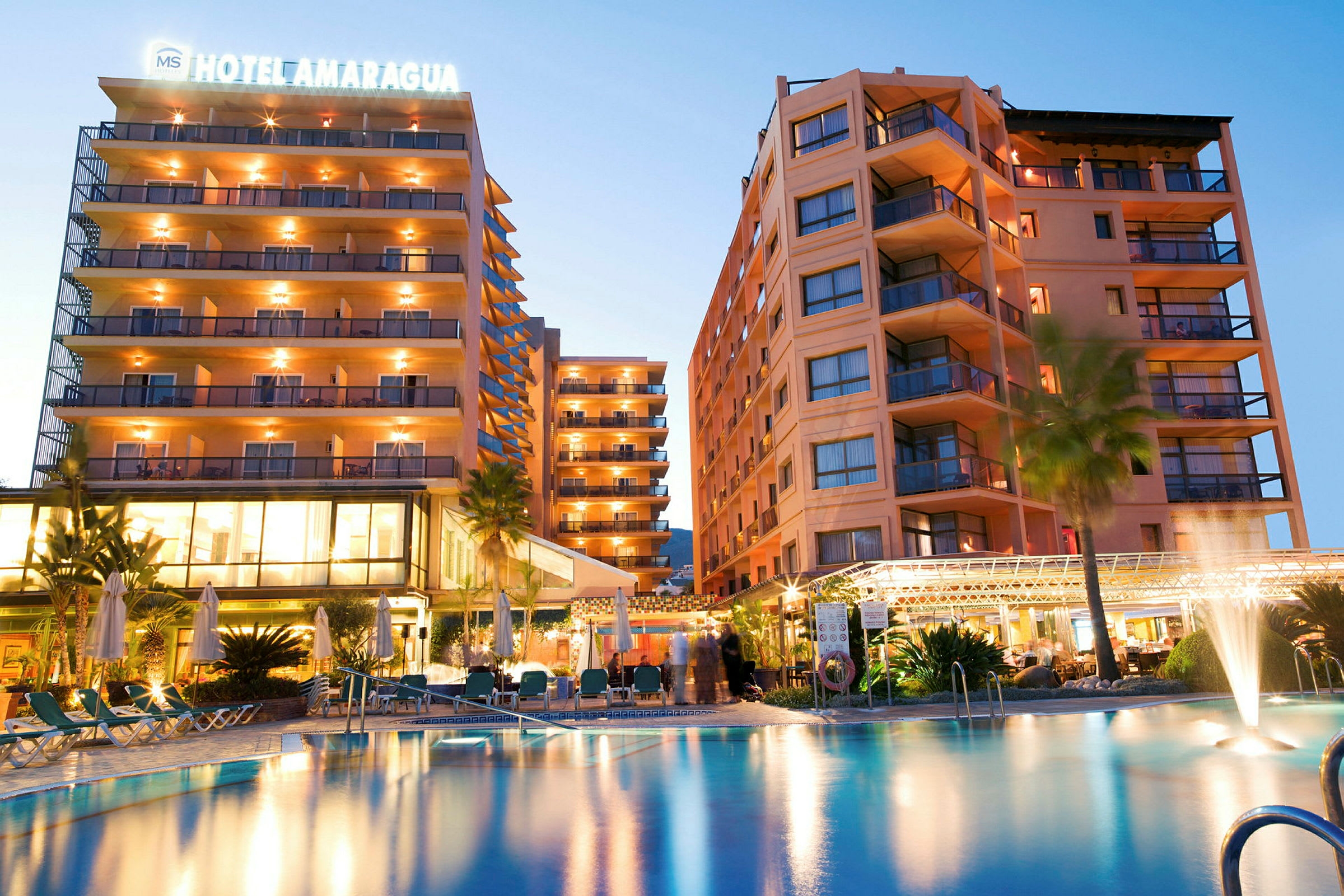 Bild av ett hotell med upplysta byggnader och en pool i förgrunden. (AI-genererad text)